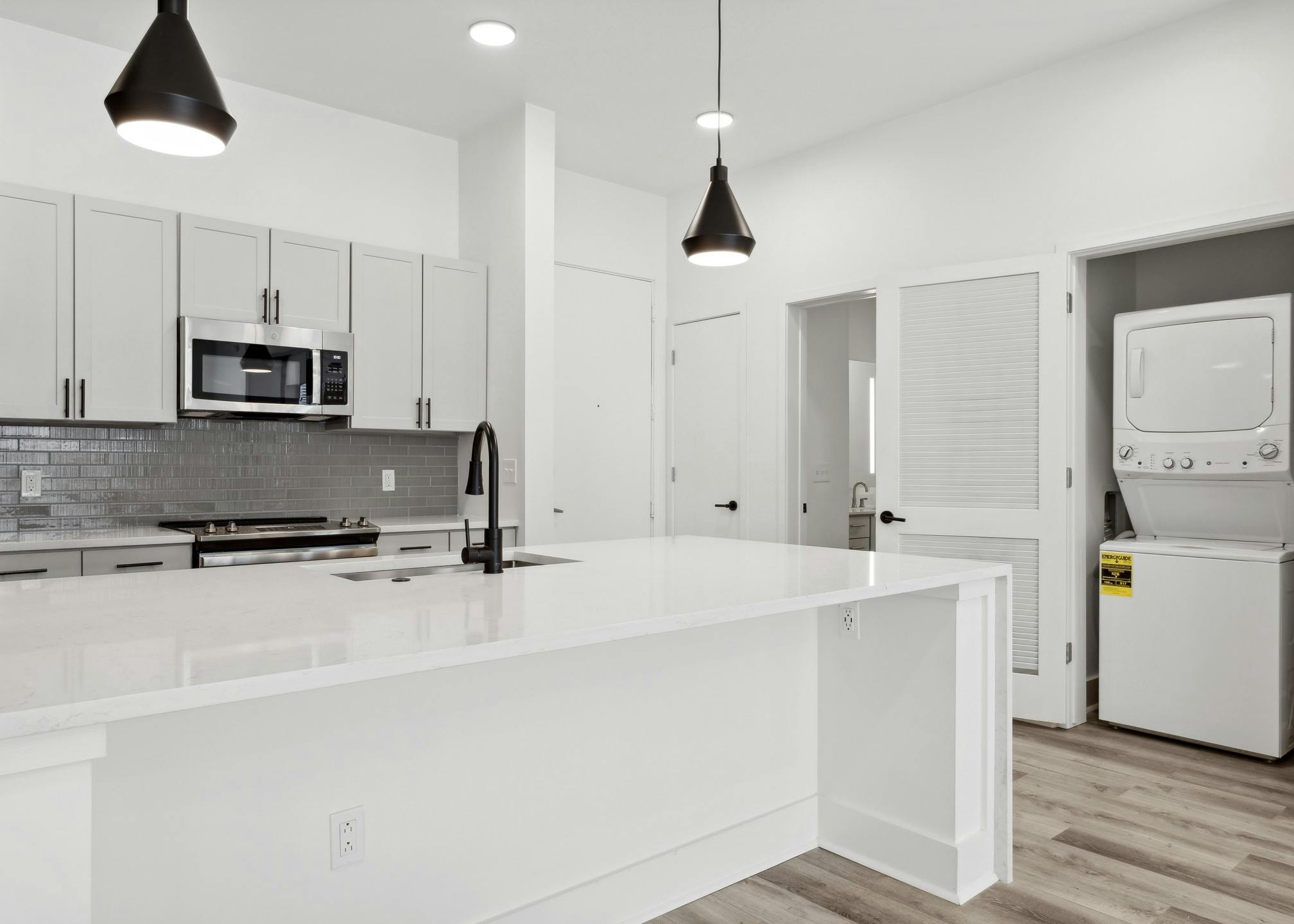 Island kitchen with white counter tops and cabinets and gray tiled backsplash with view of laundry closet at AMLI Old 4th Ward