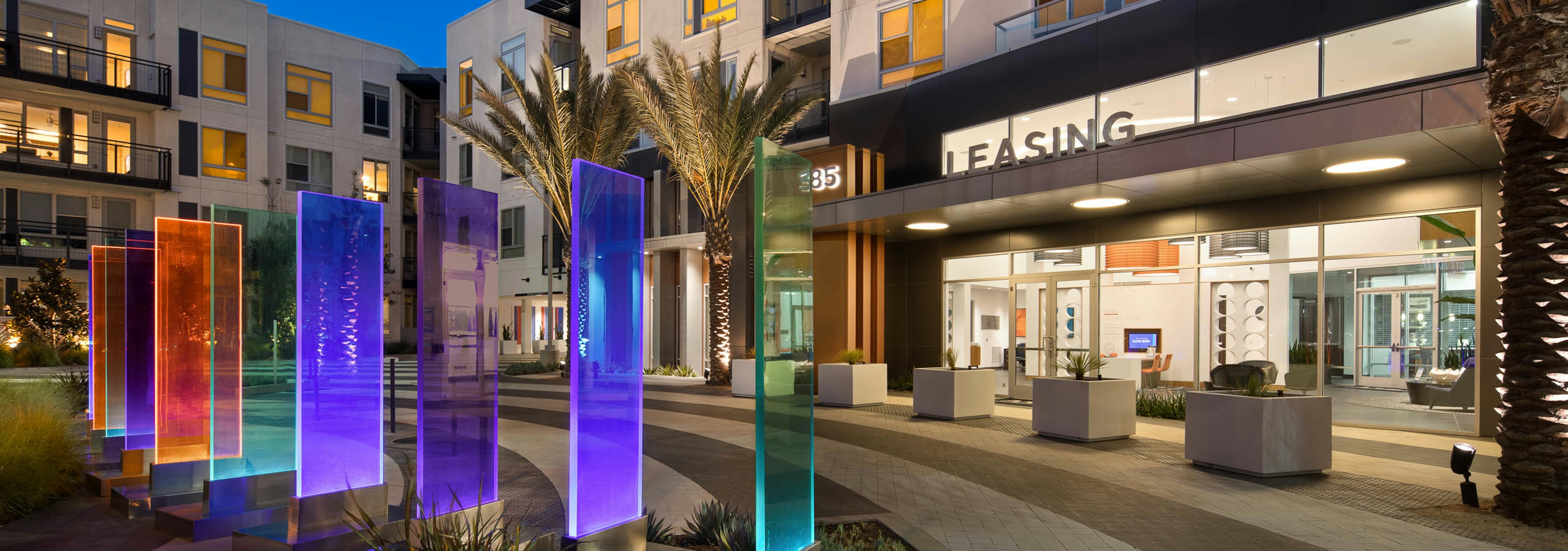 Exterior of AMLI Uptown Orange apartment building leasing office entrance facing eight-foot multi-colored glass panels