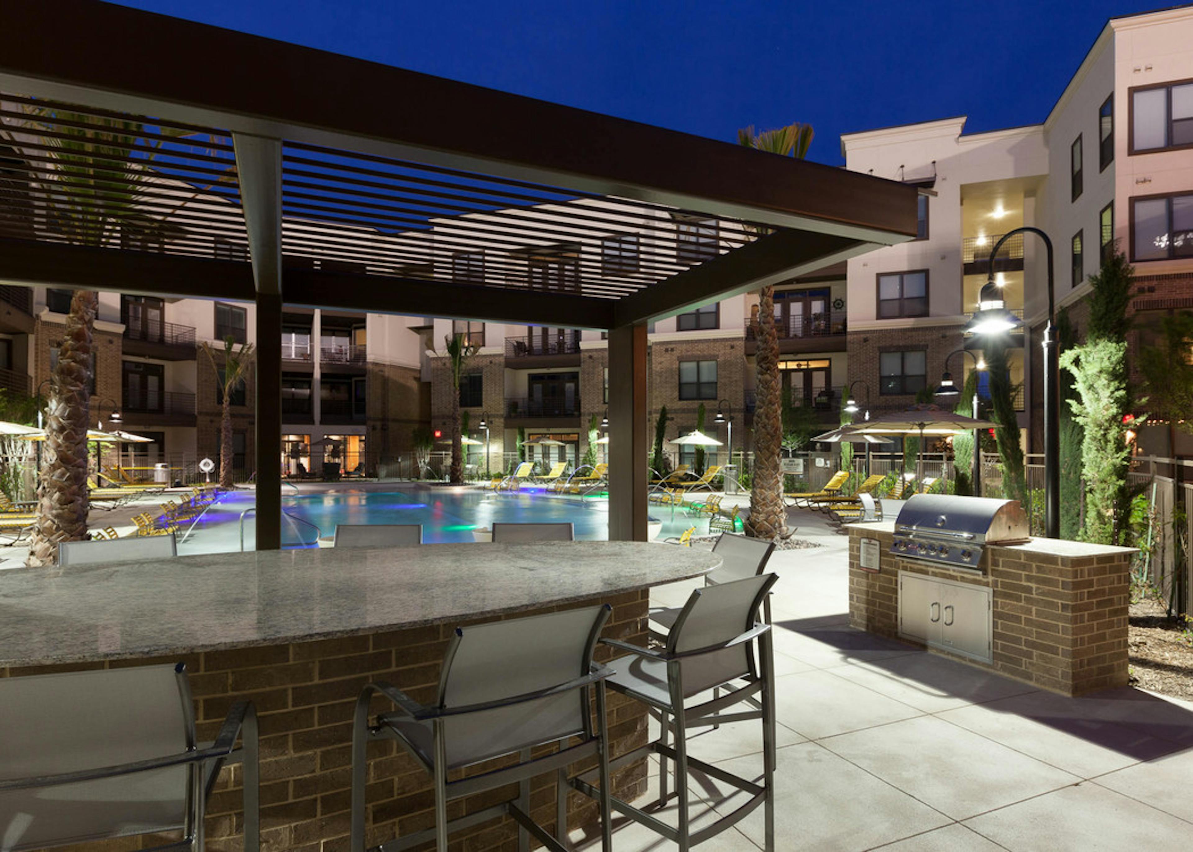Nighttime view of grill station and seating at pool area at AMLI at the Ballpark apartments with building in background