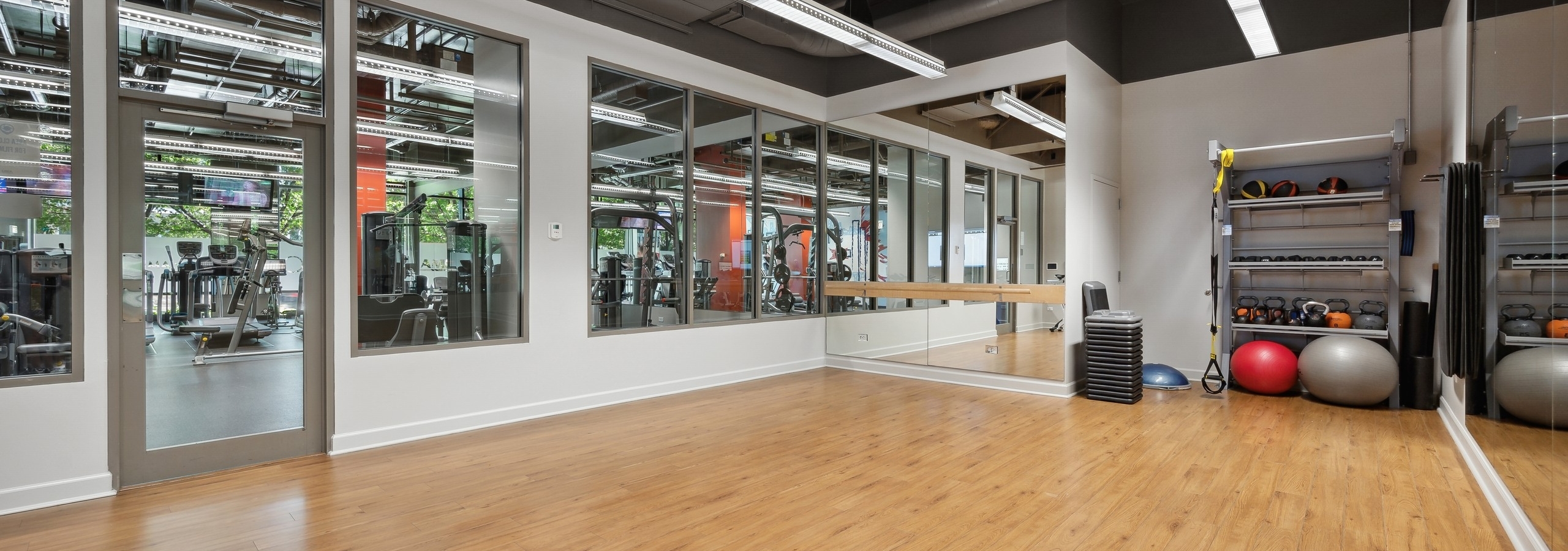 The yoga and spin room at AMLI 900 with 2 yoga balls and equipment in back corner and view to fitness center