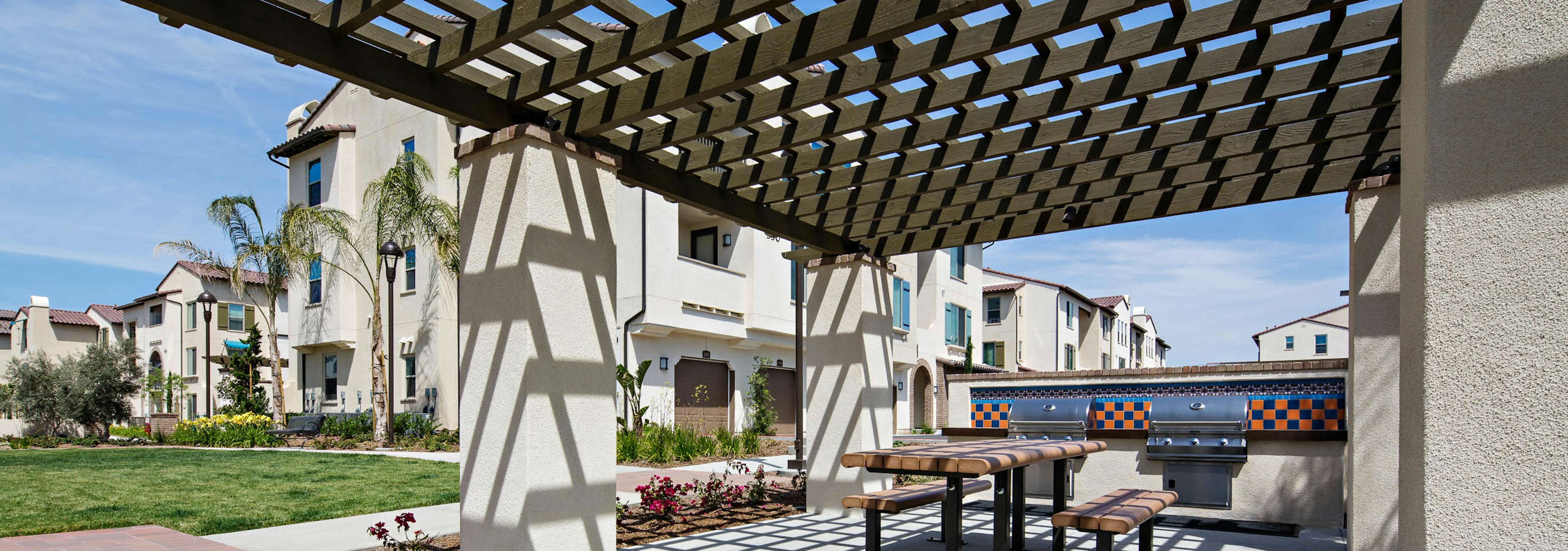 Daytime view of AMLI Spanish Hills apartment building wood pergola with grill station, picnic table and lush landscaping