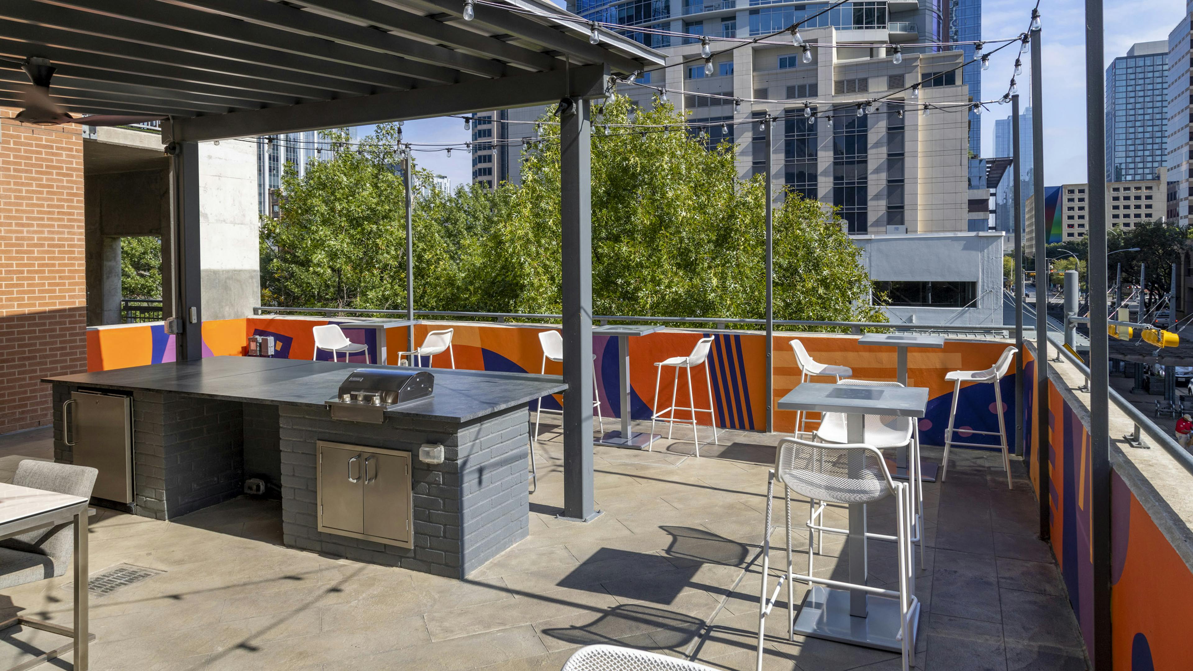 AMLI Downtown outdoor grill deck with white tall chairs and string lights surrounded by Austin skyscrapers and trees