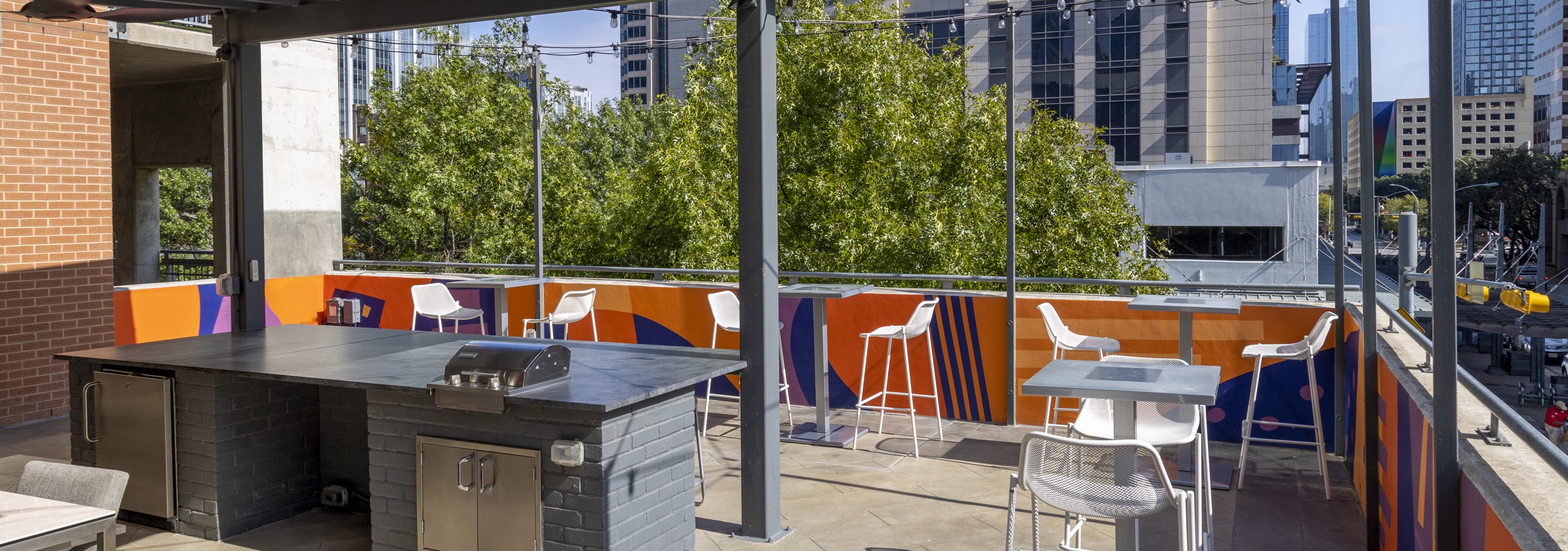 AMLI Downtown outdoor grill deck with white tall chairs and string lights surrounded by Austin skyscrapers and trees