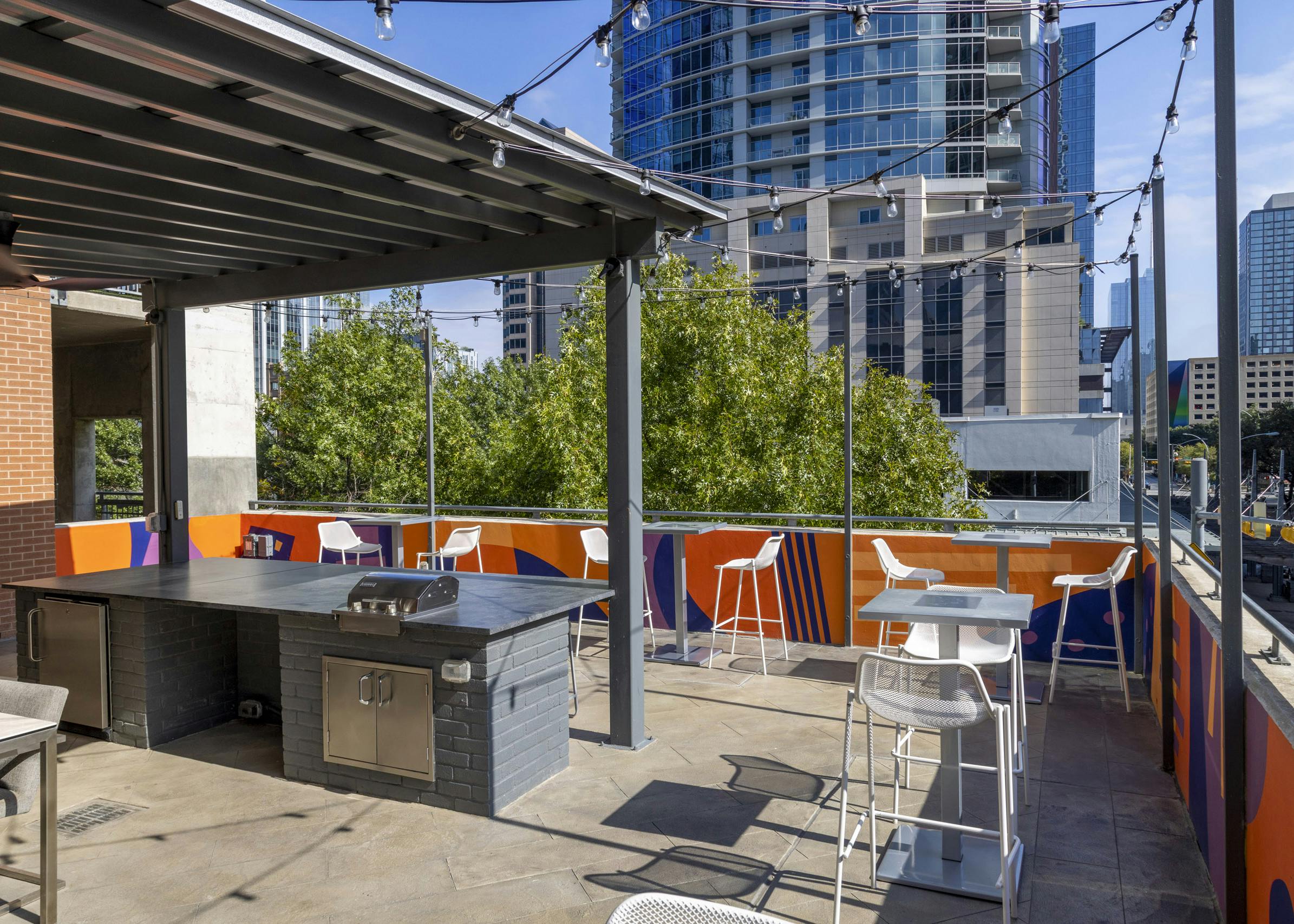 AMLI Downtown outdoor grill deck with white tall chairs and string lights surrounded by Austin skyscrapers and trees