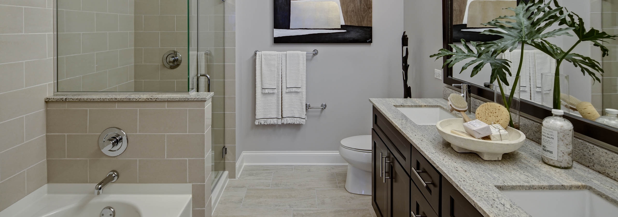 AMLI River North apartment bathroom with beige tiled bathtub and stand up shower with light tile flooring and dark cabinetry
