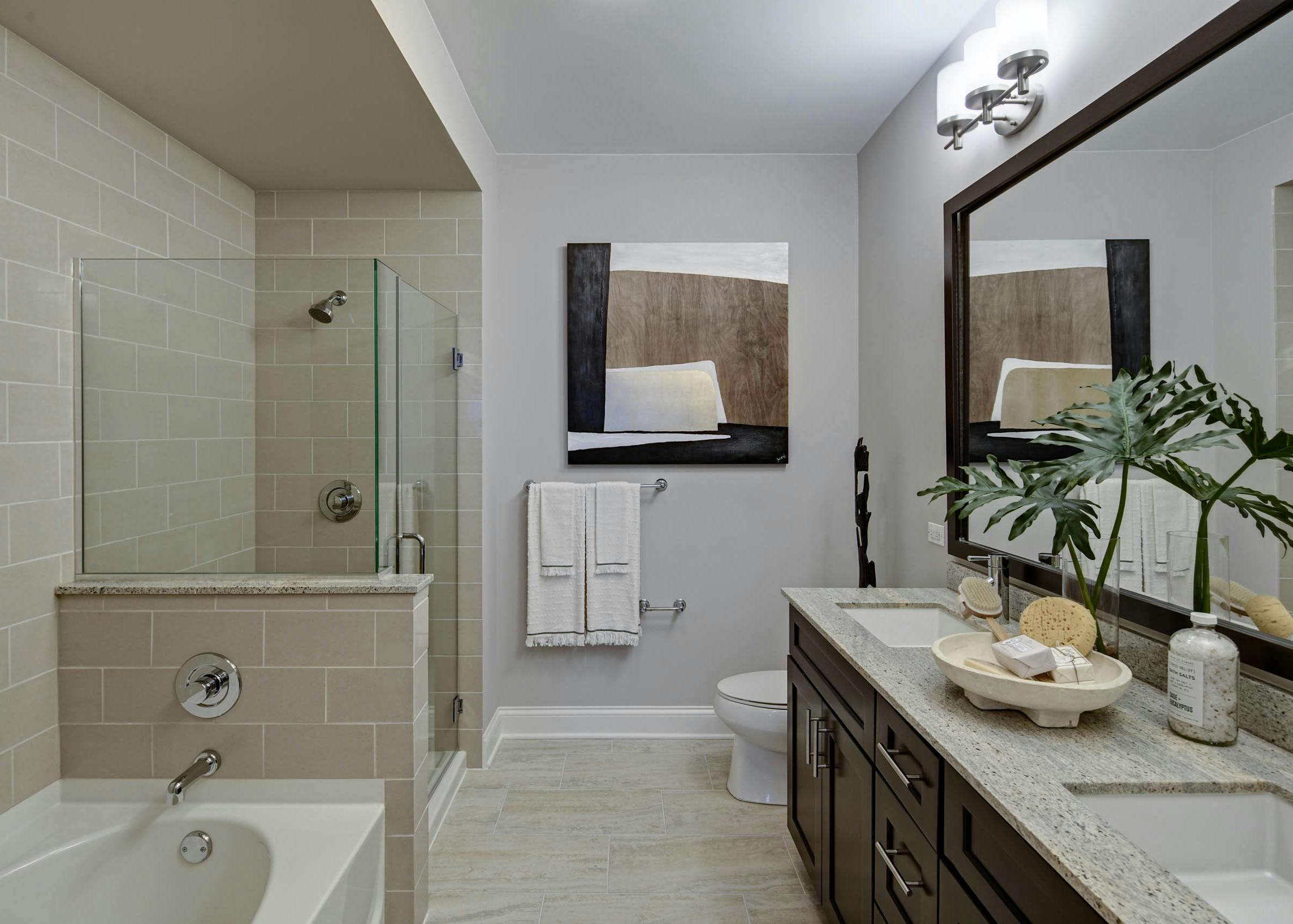 AMLI River North apartment bathroom with beige tiled bathtub and stand up shower with light tile flooring and dark cabinetry