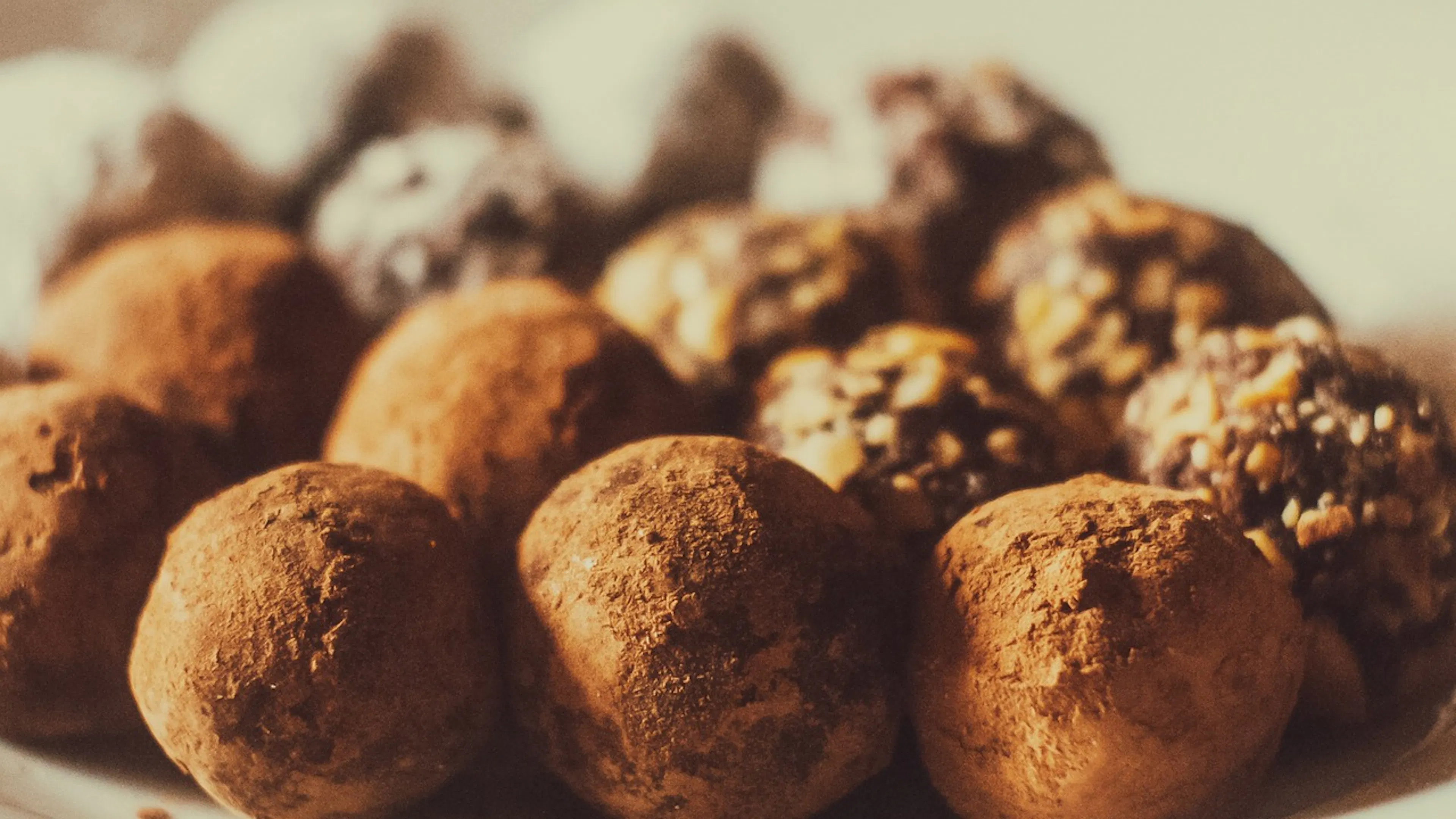 A plate of chocolate truffles covered in cocoa powder and ground walnuts and powdered sugar