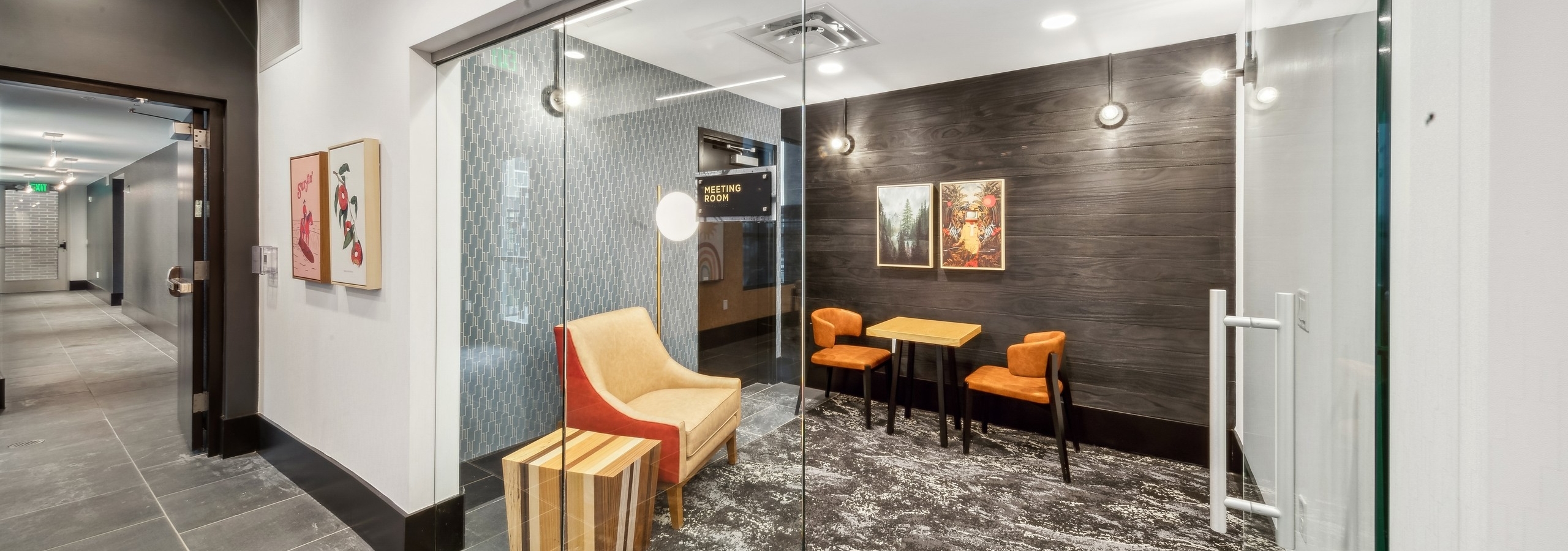 AMLI RiNo business center meeting room with a glass door and guest chair and wood table with 2 chairs on dark paneled wall