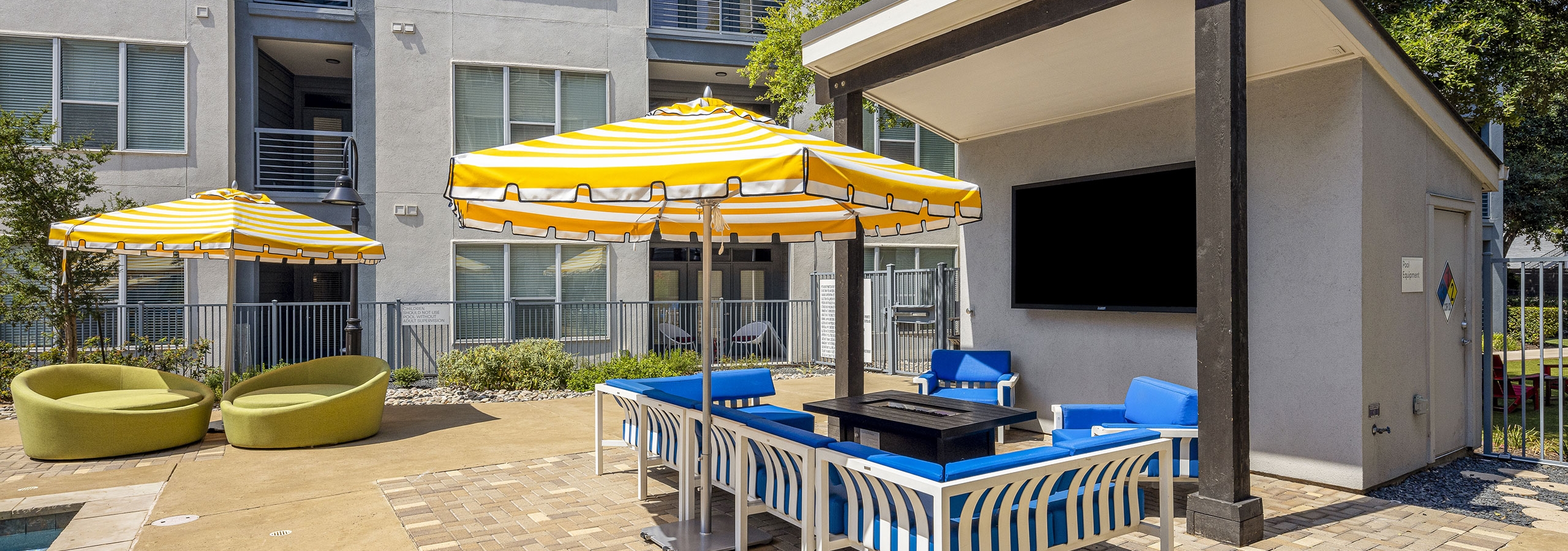 AMLI South Shore poolside cabana with big screen TV surrounded by blue furniture and 2 yellow and white umbrellas