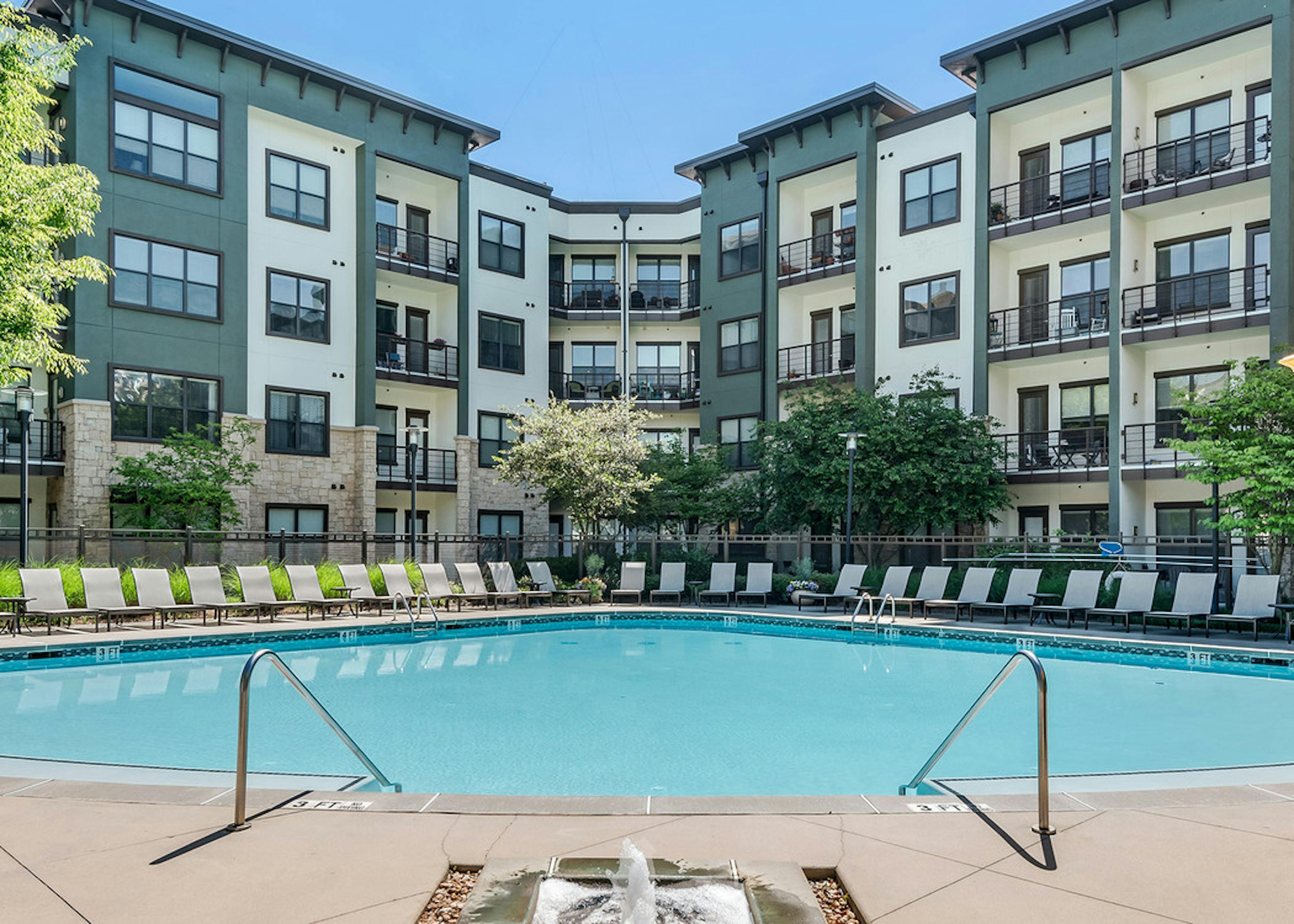 Exterior view of pool at AMLI Parkside surrounded by white lounge chairs with building straight ahead of it on a sunny day
