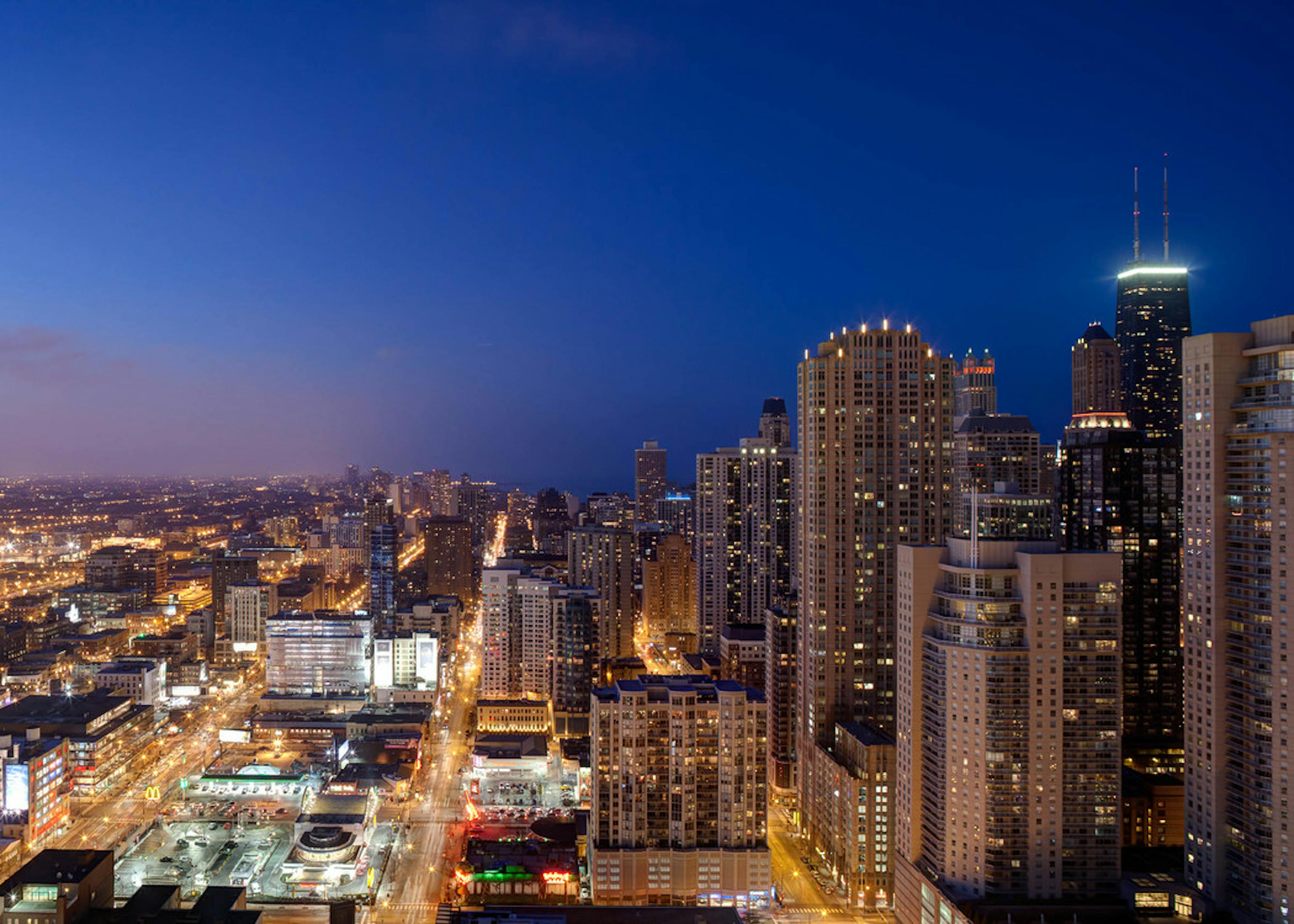 Nightime shot of downtown Chicago with lit skyscrapers and deep blue sky.