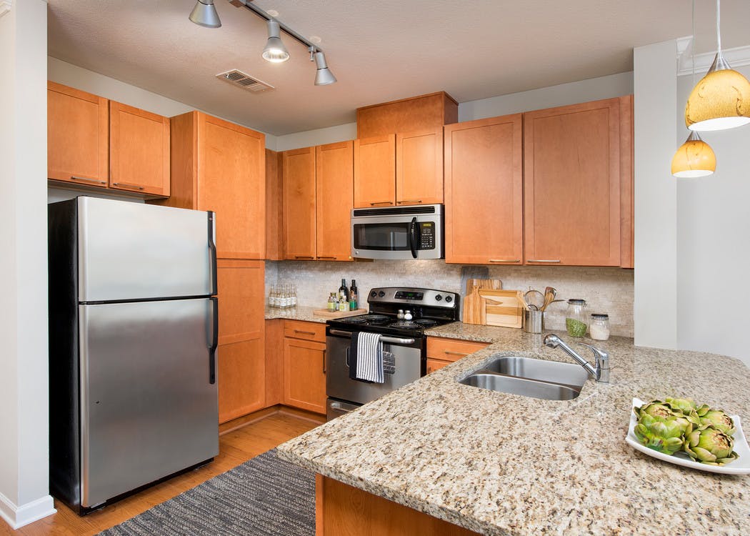 AMLI North Point kitchen with medium colored wood cabinets and stainless steel appliances with spacious granite countertops