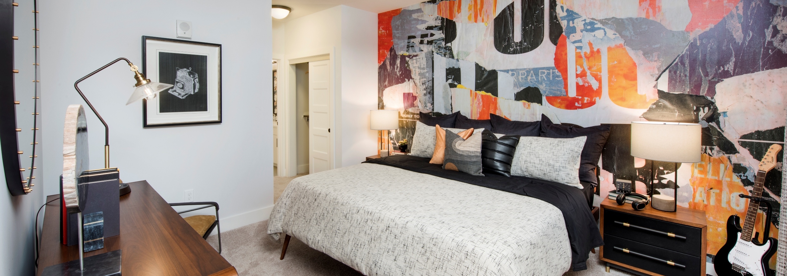 Interior of AMLI Decatur bedroom with bed centered on colorful patterned wall with furniture on left wall and ceiling fan