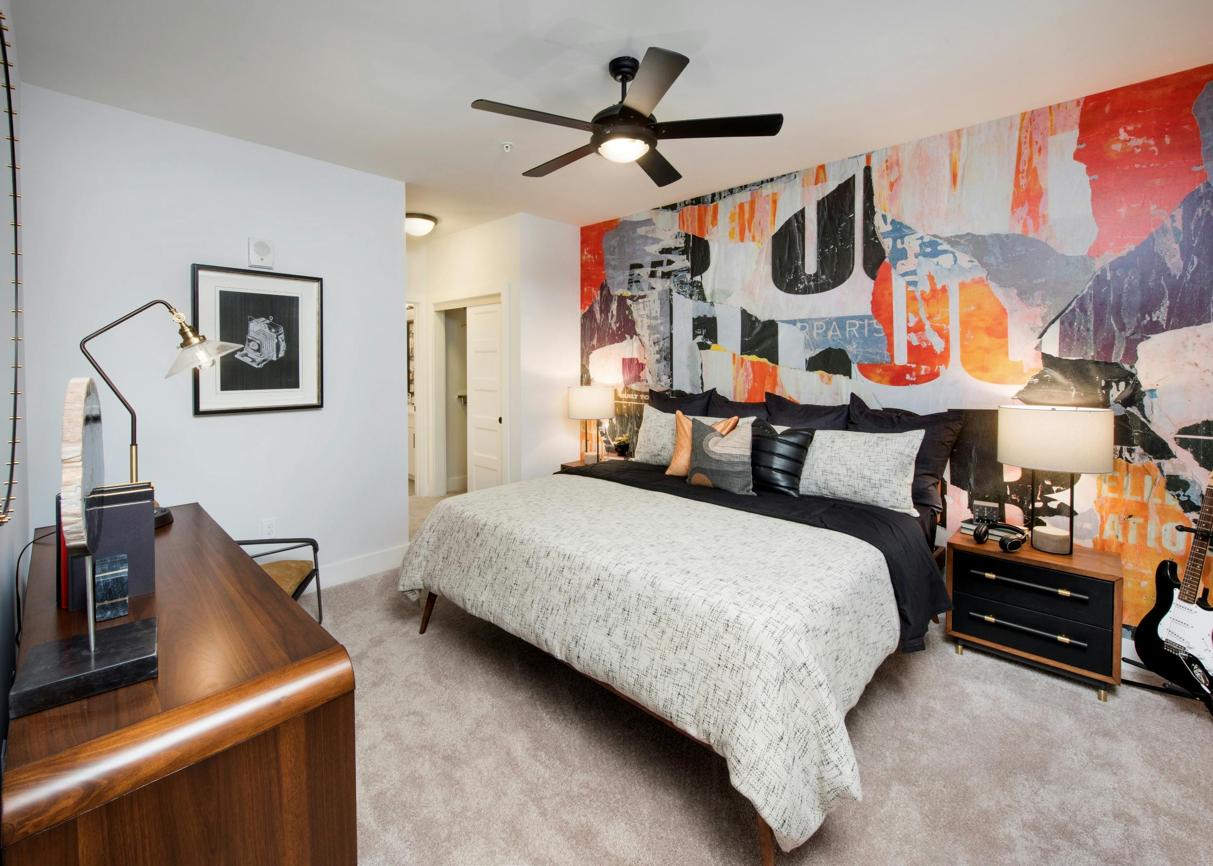 Interior view of AMLI Dectaur apartment bedroom with bed centered on colorful wall and furniture on left wall and ceiling fan