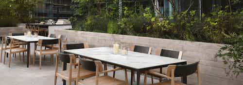 AMLI Fountain Place outdoor dining area with two white marble top tables with chairs and lush green trees and hanging lights