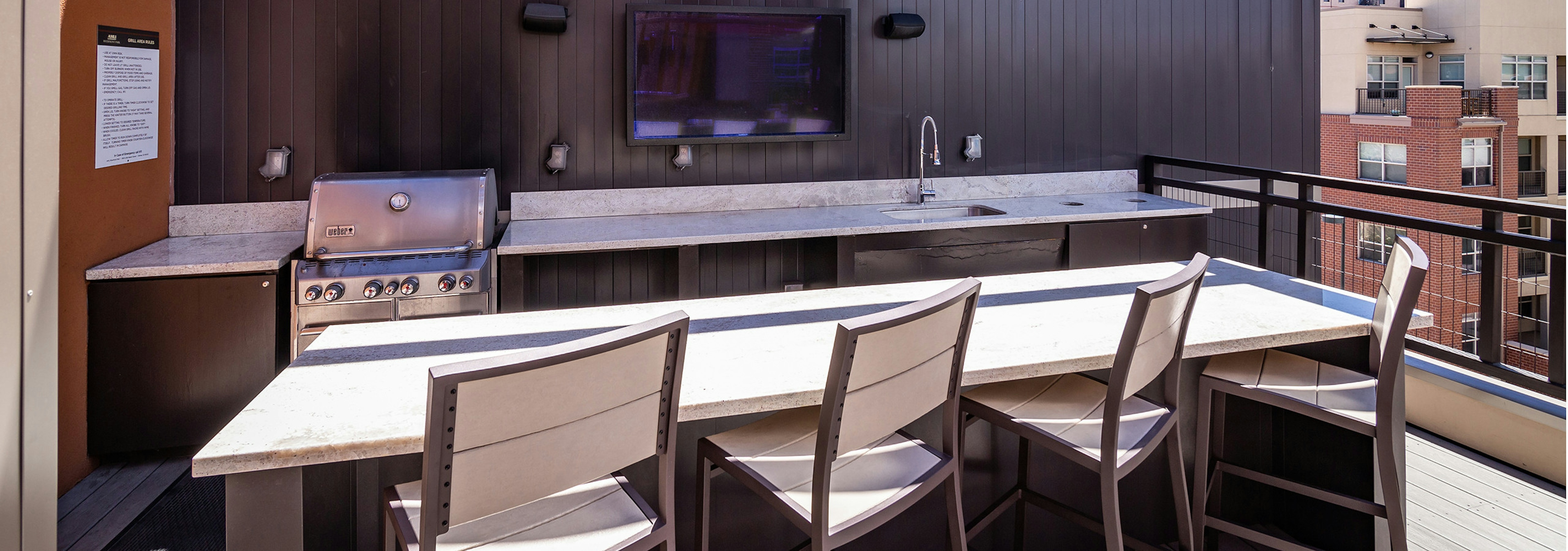 A rooftop grill area at AMLI Riverfront Park apartments with a television and a sink as well as a counter top with bar chairs