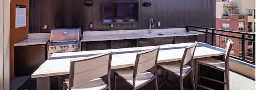 A rooftop grill area at AMLI Riverfront Park apartments with a television and a sink as well as a counter top with bar chairs