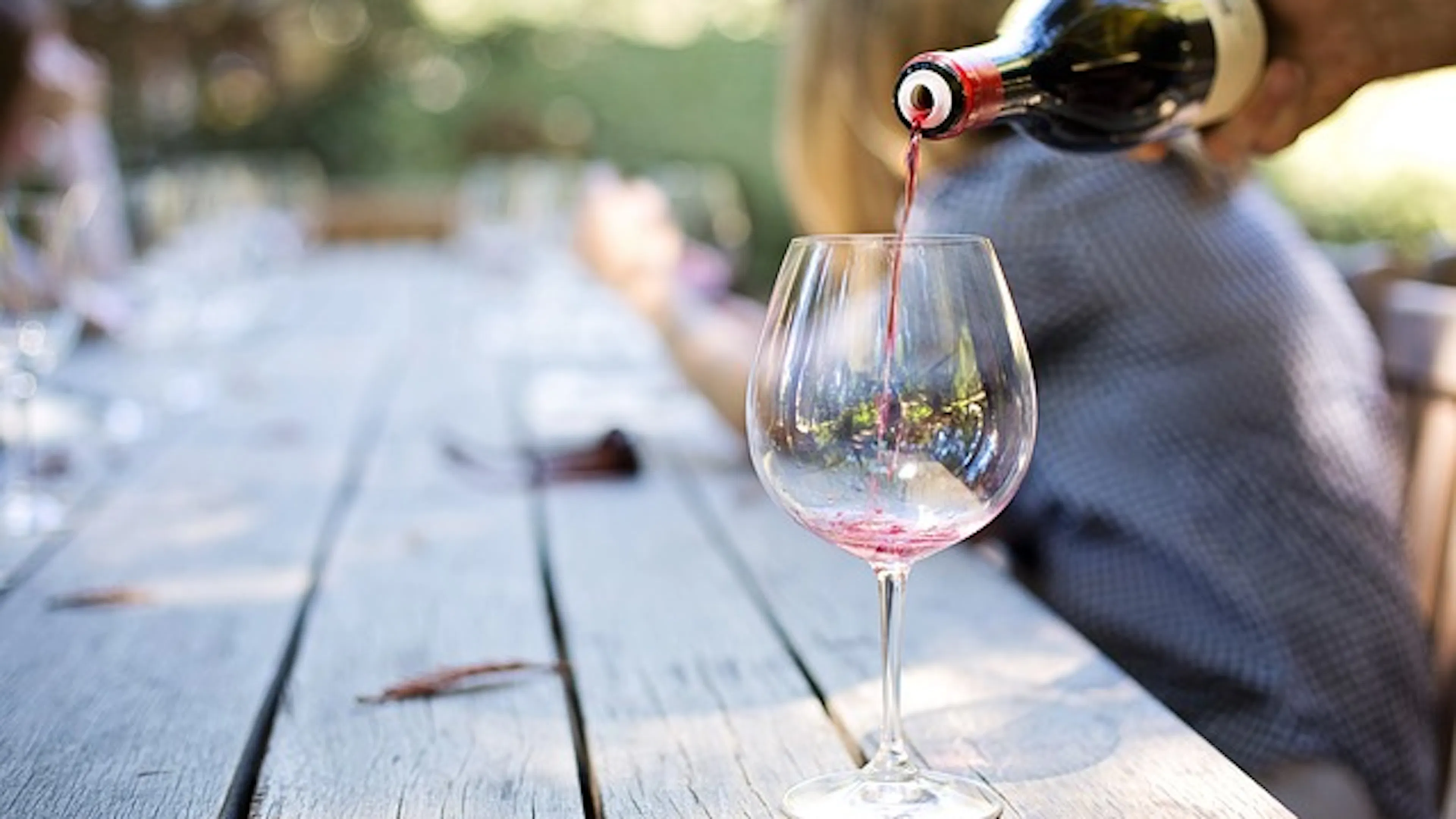 A wine glass being filled with red wine on a large wooden outdoor table