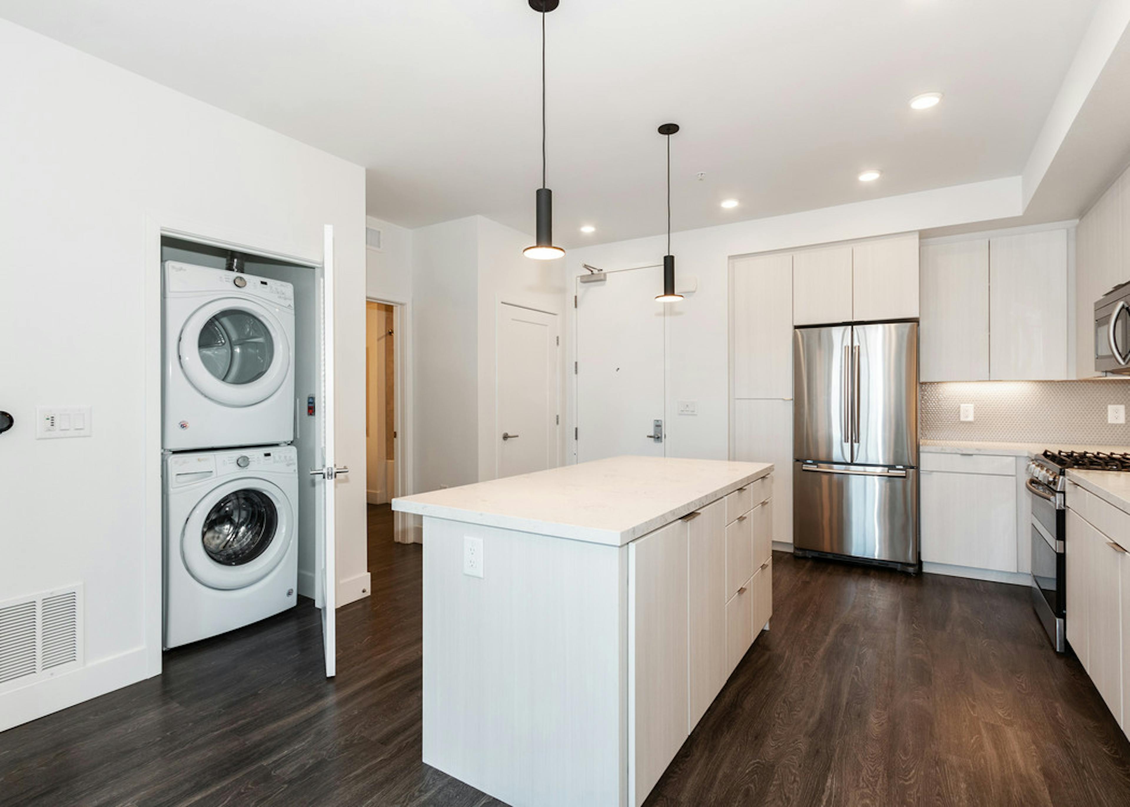 Interior of AMLI Park Broadway apartment kitchen with white cabinetry, stainless steel appliances and full washer and dryer