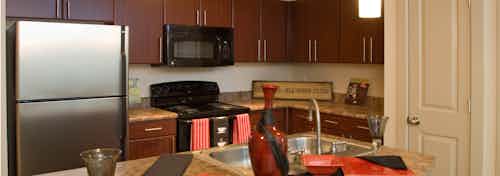 Interior view of kitchen at AMLI Inverness apartments with island and pottery and fridge and microwave with espresso cabinets