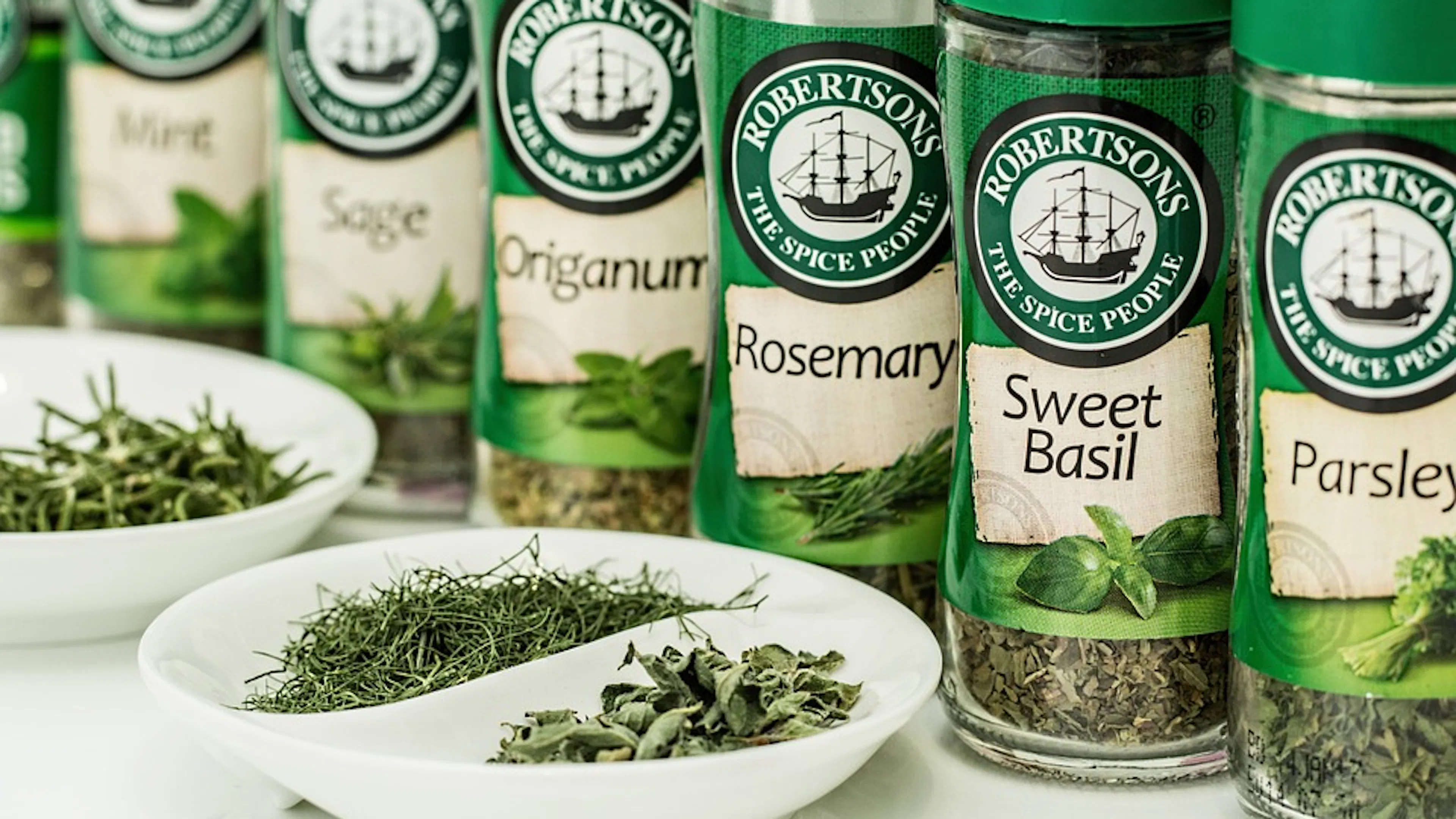 Seven jars of herbs filled with mint sage oregano rosemary basil and parsley