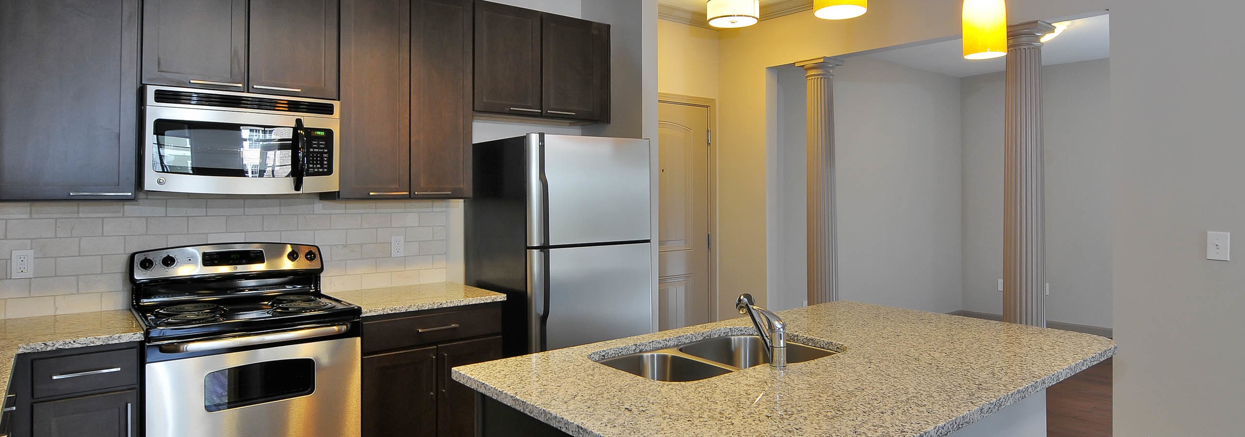 AMLI North Point kitchen with a wide island and dark cabinets with granite countertops and a neutral tiled backsplash