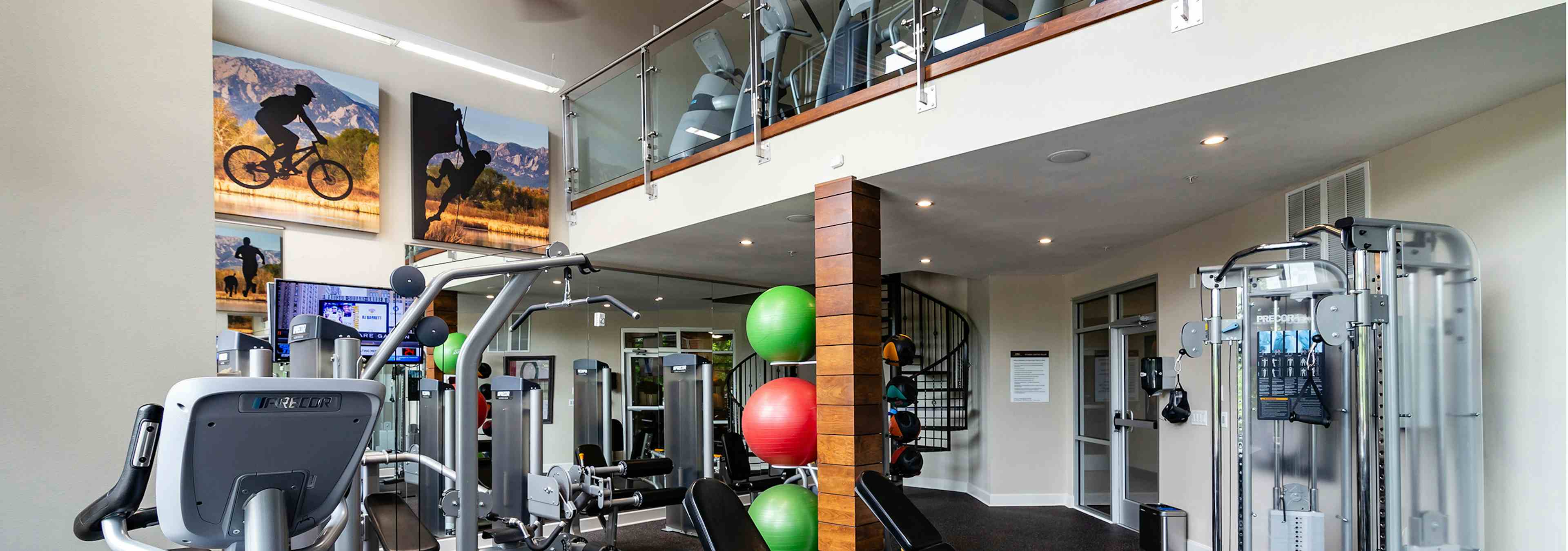 View of two story fitness center at AMLI Riverfront Park apartments with free weights and other strength training machines