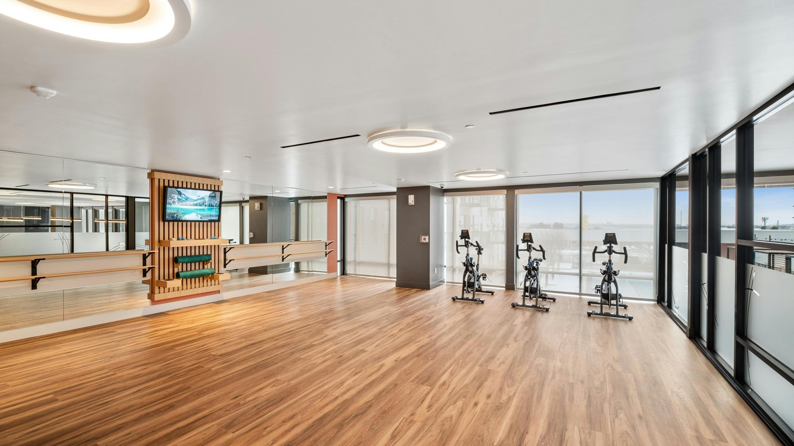Yoga spin studio at AMLI Broadway Park with hardwood flooring and stationary bikes as well as ballet bara and shaded windows