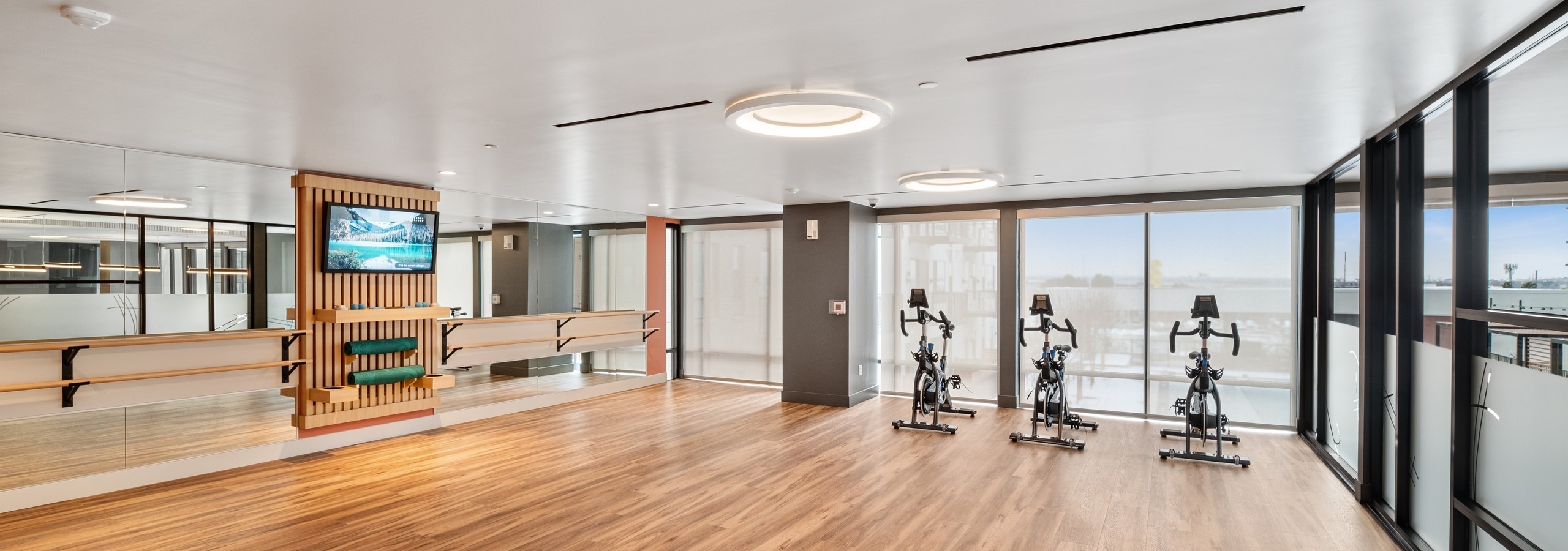 Yoga spin studio at AMLI Broadway Park with hardwood flooring and stationary bikes as well as ballet bara and shaded windows