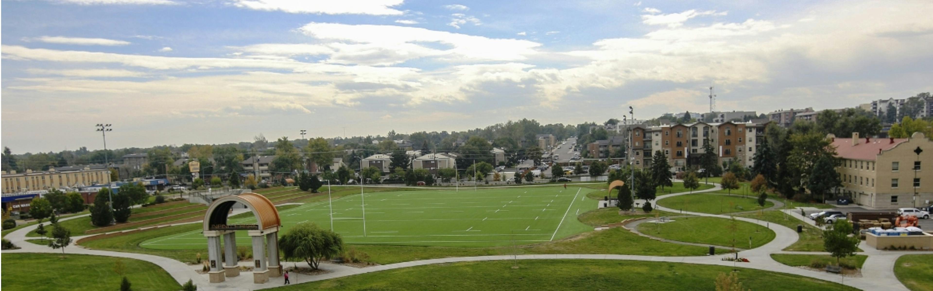 A view of a football field in Glendale Colorado with surrounding building and sidewalks and trees with a blue sky and clouds