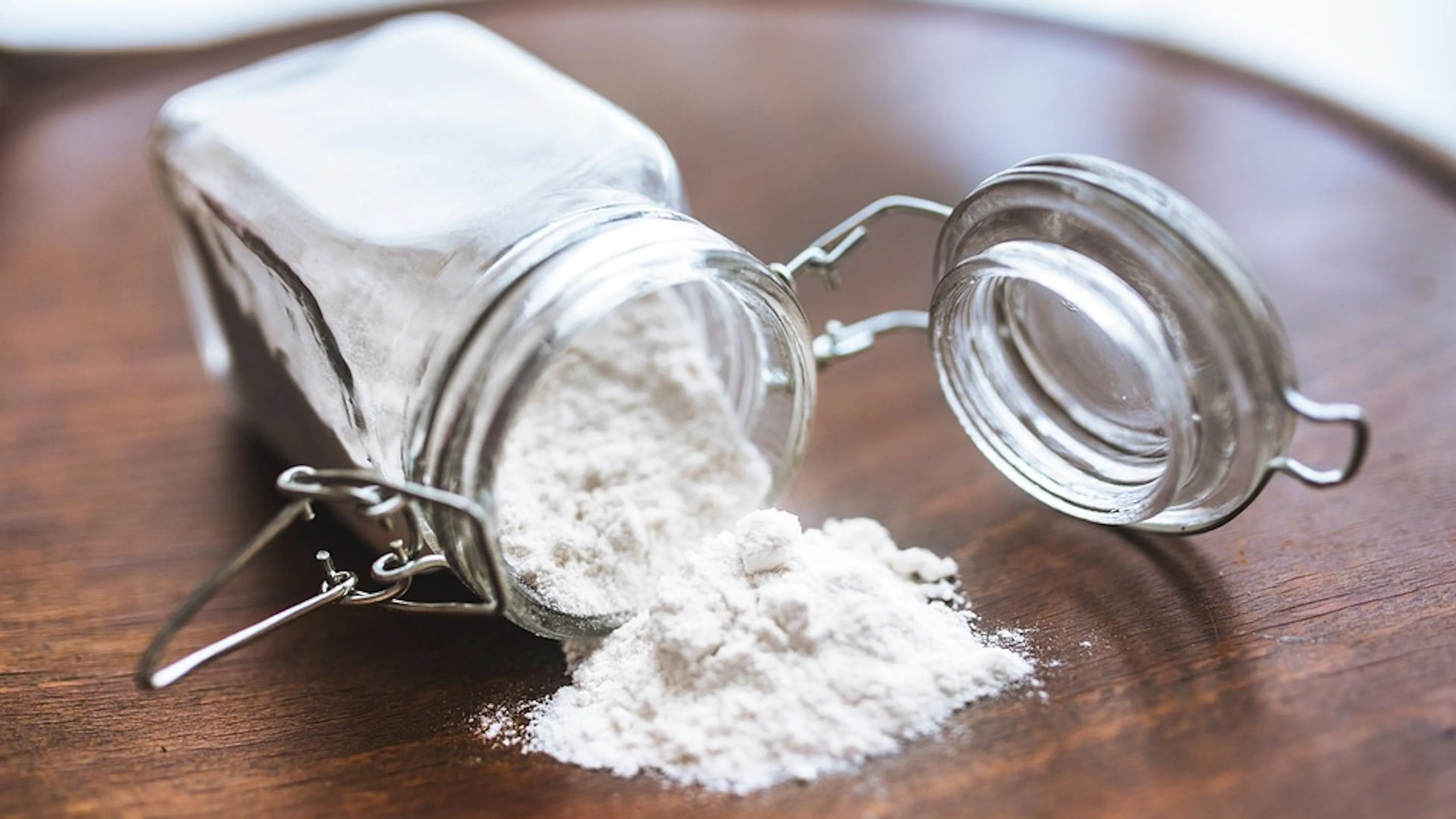 A small glass jar filled with flour tipped over onto a wooden tray