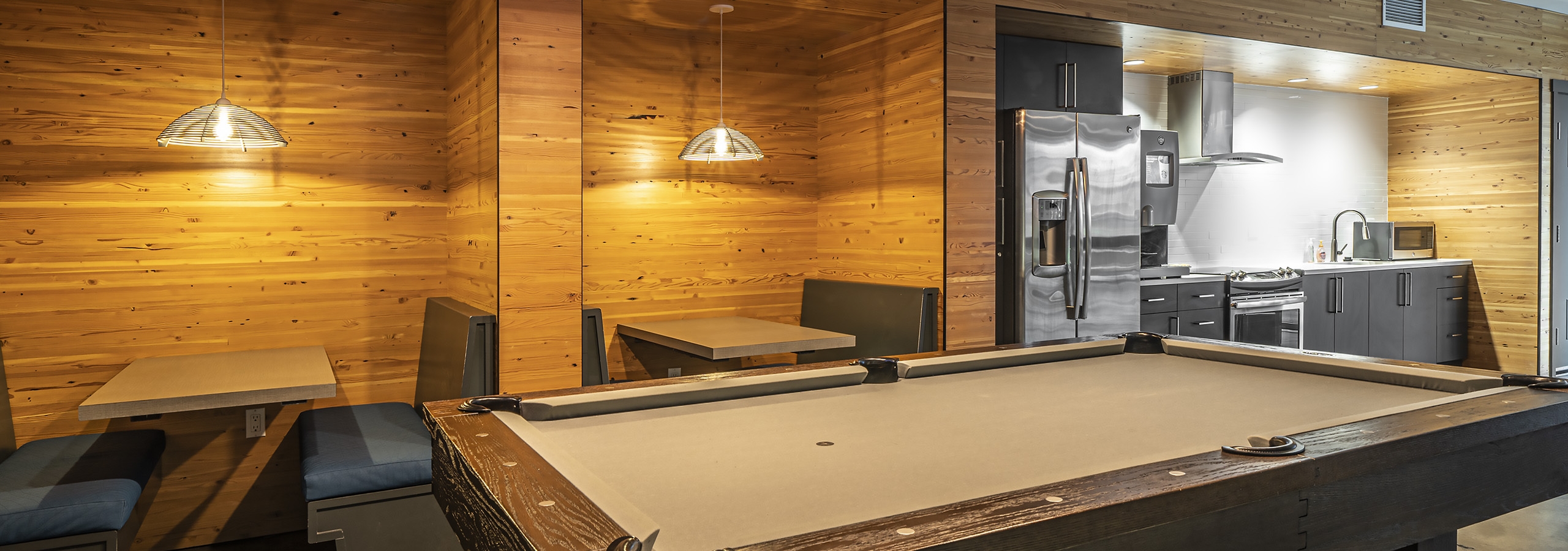 Interior view of clubroom AMLI Mark24 with booth seating and billiards table and kitchen with stainless steel appliances
