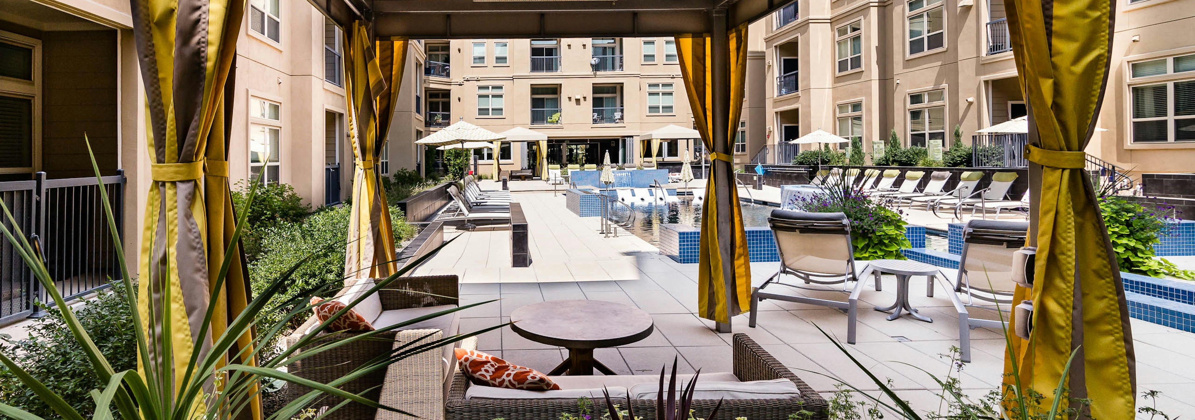 Daytime view of AMLI RidgeGate apartments landscaped pool deck from personal curtained cabana with plentiful lounge seating 