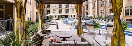 Daytime view of AMLI RidgeGate apartments landscaped pool deck from personal curtained cabana with plentiful lounge seating