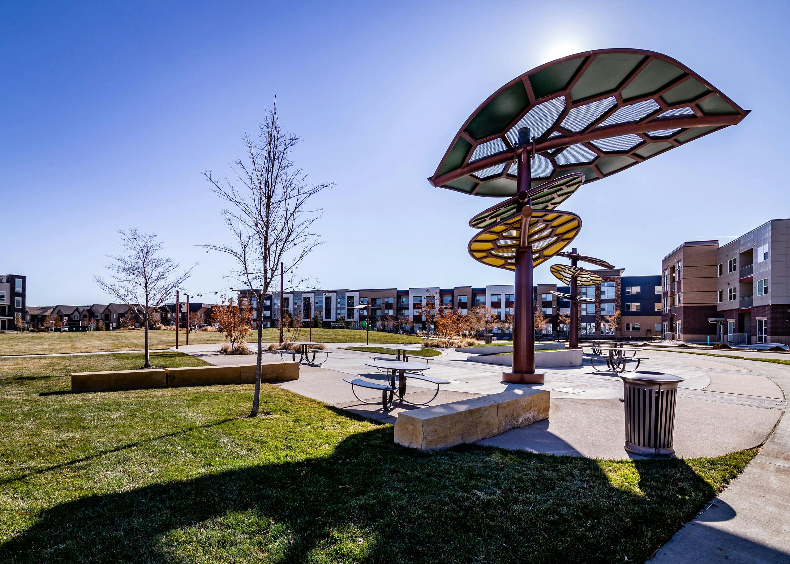 Daytime view of AMLI Littleton Village apartment building adjacent to 3.5-acre park with leaf canopies and festoon lighting