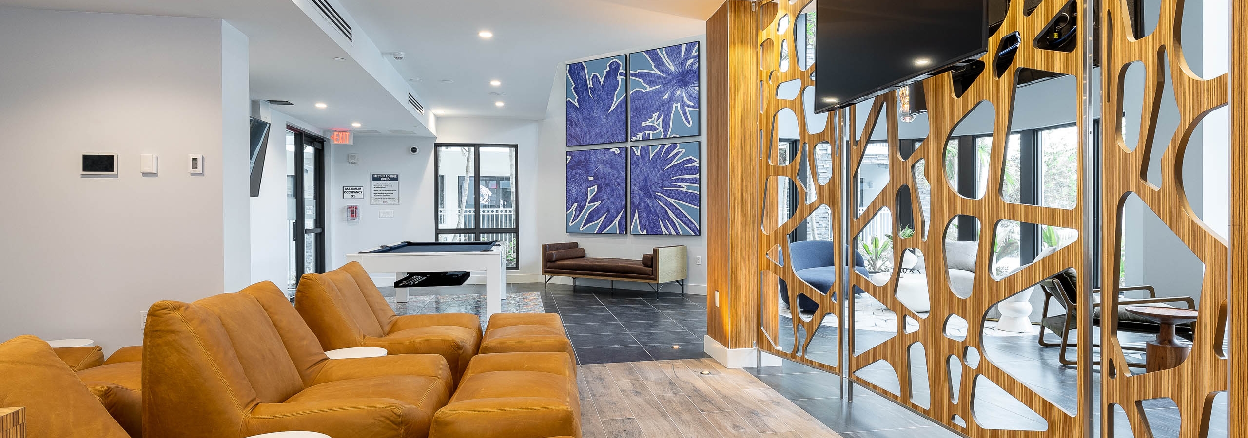 AMLI Park West apartment resident lounge with oversized armchairs facing a mounted TV and pool table with blue wall artwork