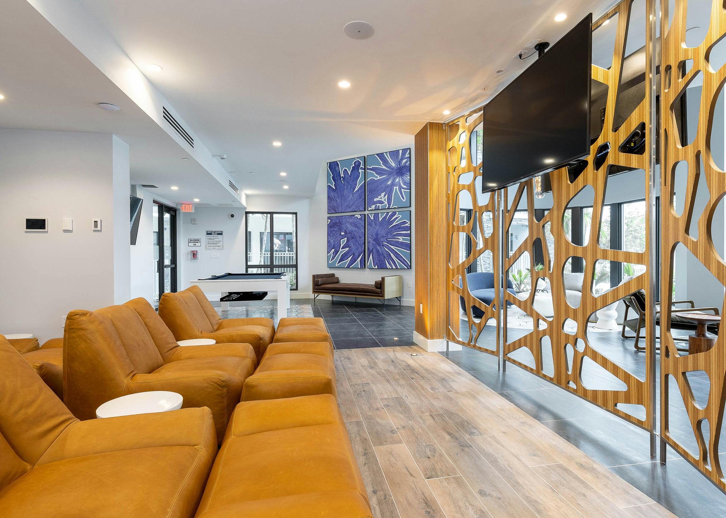 AMLI Park West apartment resident lounge with oversized armchairs facing a mounted TV and pool table with blue wall artwork