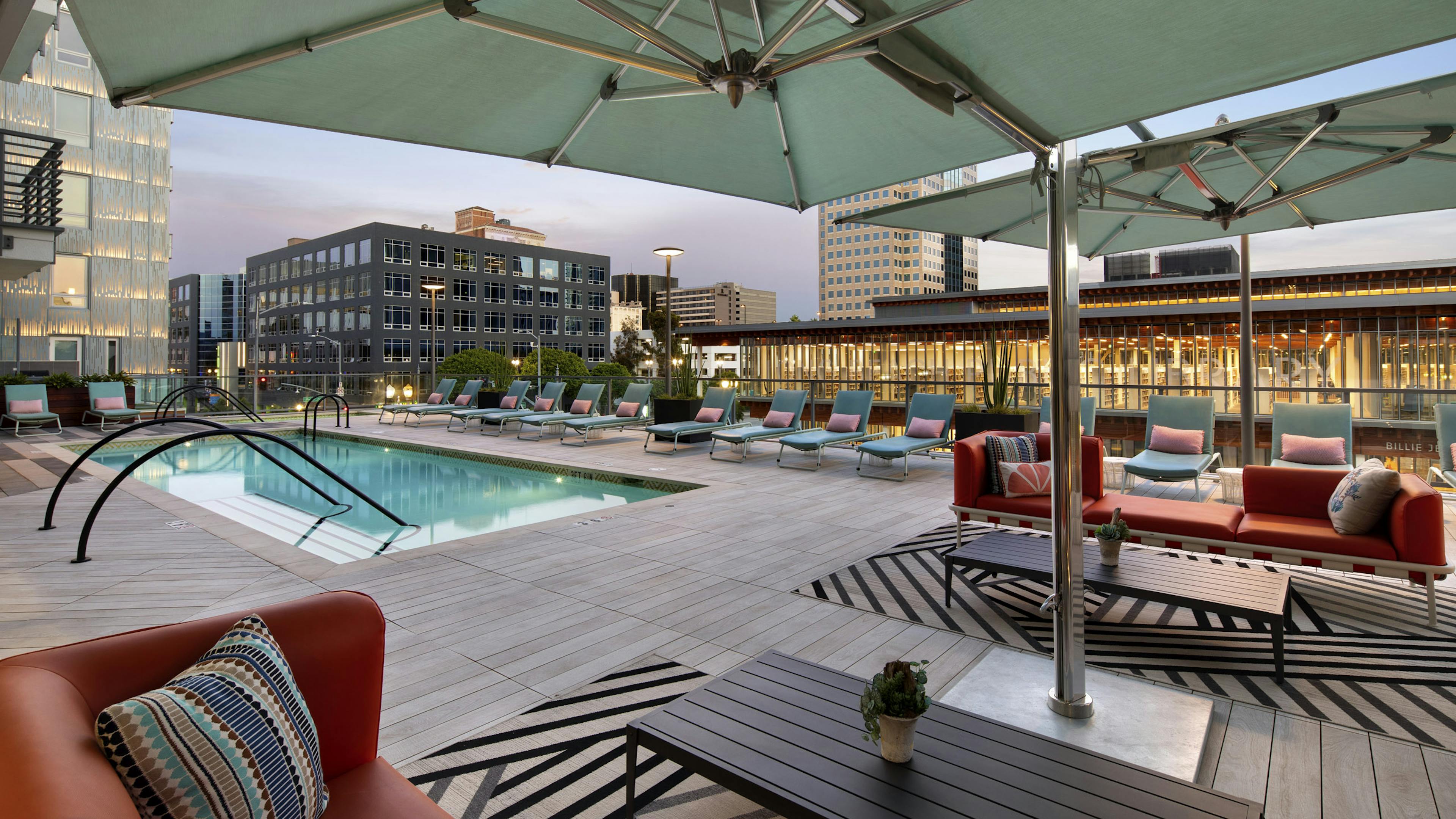 Dusk view of AMLI Park Broadway pool deck with colorful lounge and couch seating and umbrellas overlooking the city