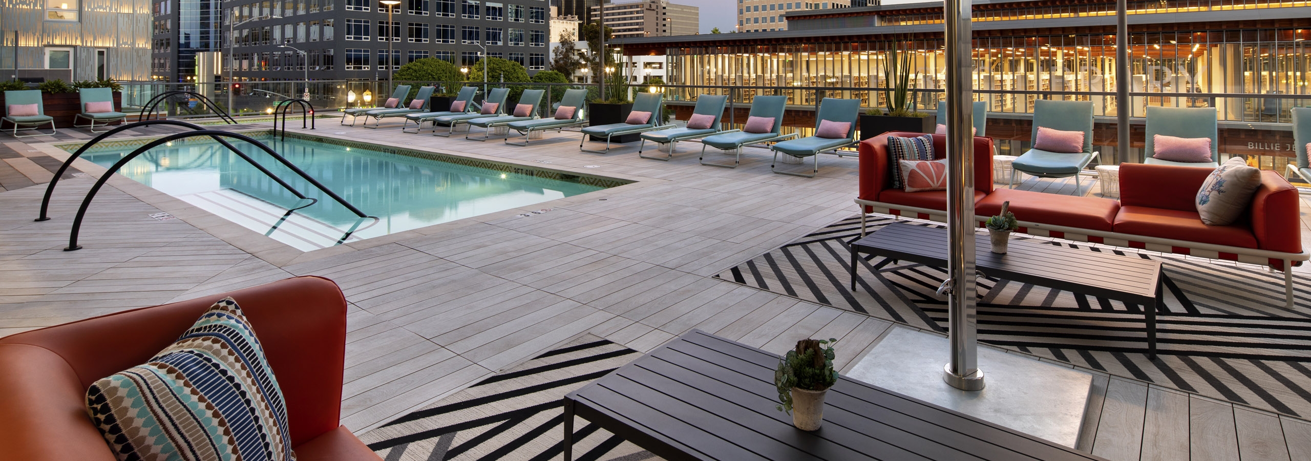 Dusk view of AMLI Park Broadway pool deck with colorful lounge and couch seating and umbrellas overlooking the city