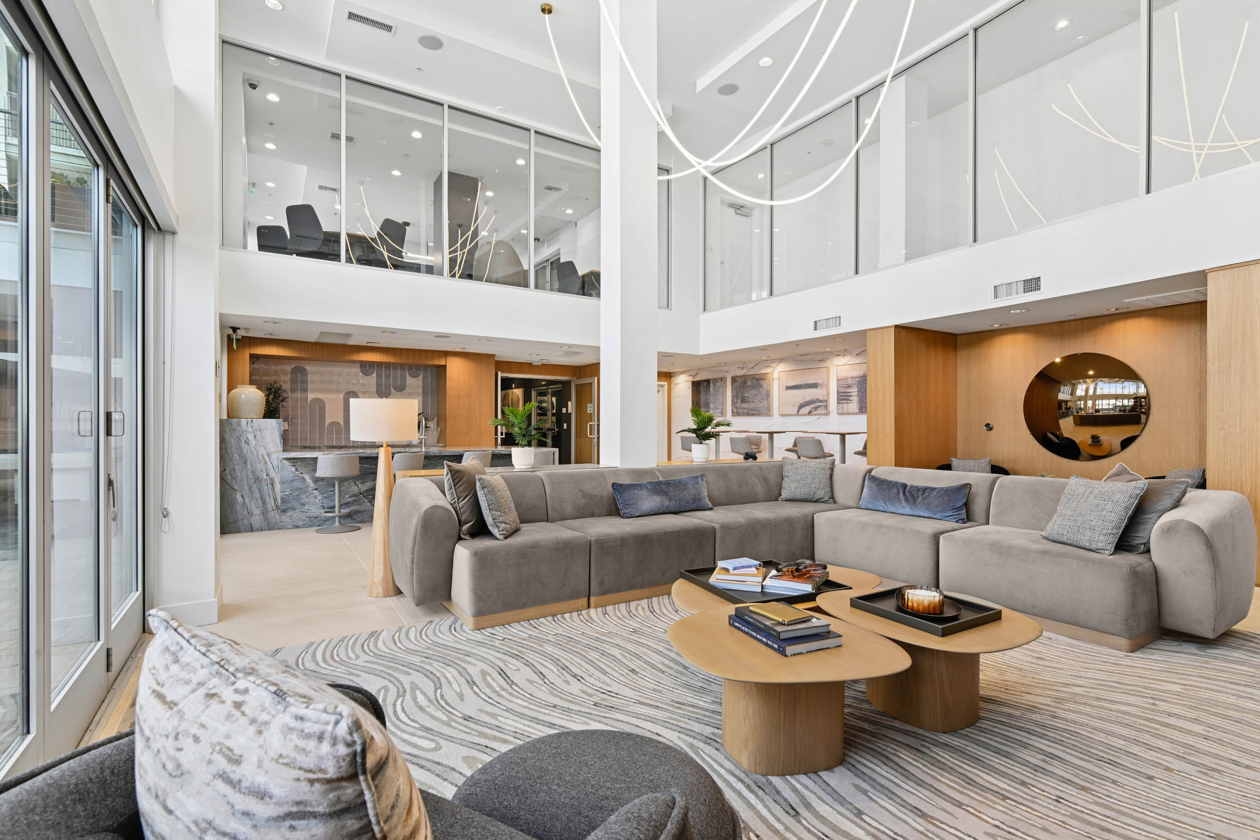 Clubroom at AMLI Lex on Orange with high ceilings, a large gray sectional, wood coffee tables, and a swirl-patterned rug, with a stone counter with stools and wood-paneled walls.