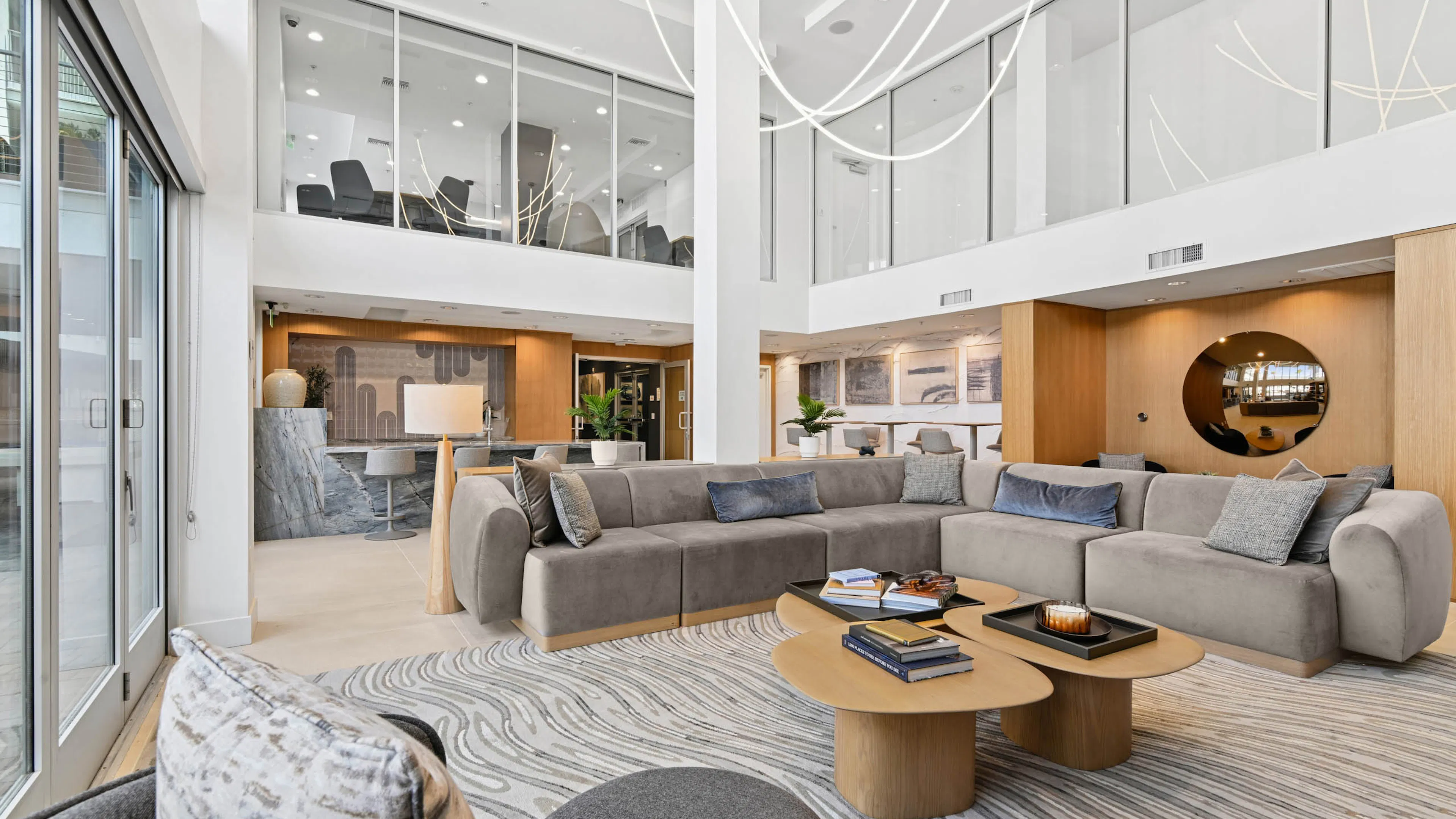Clubroom at AMLI Lex on Orange with high ceilings, a large gray sectional, wood coffee tables, and a swirl-patterned rug, with a stone counter with stools and wood-paneled walls.