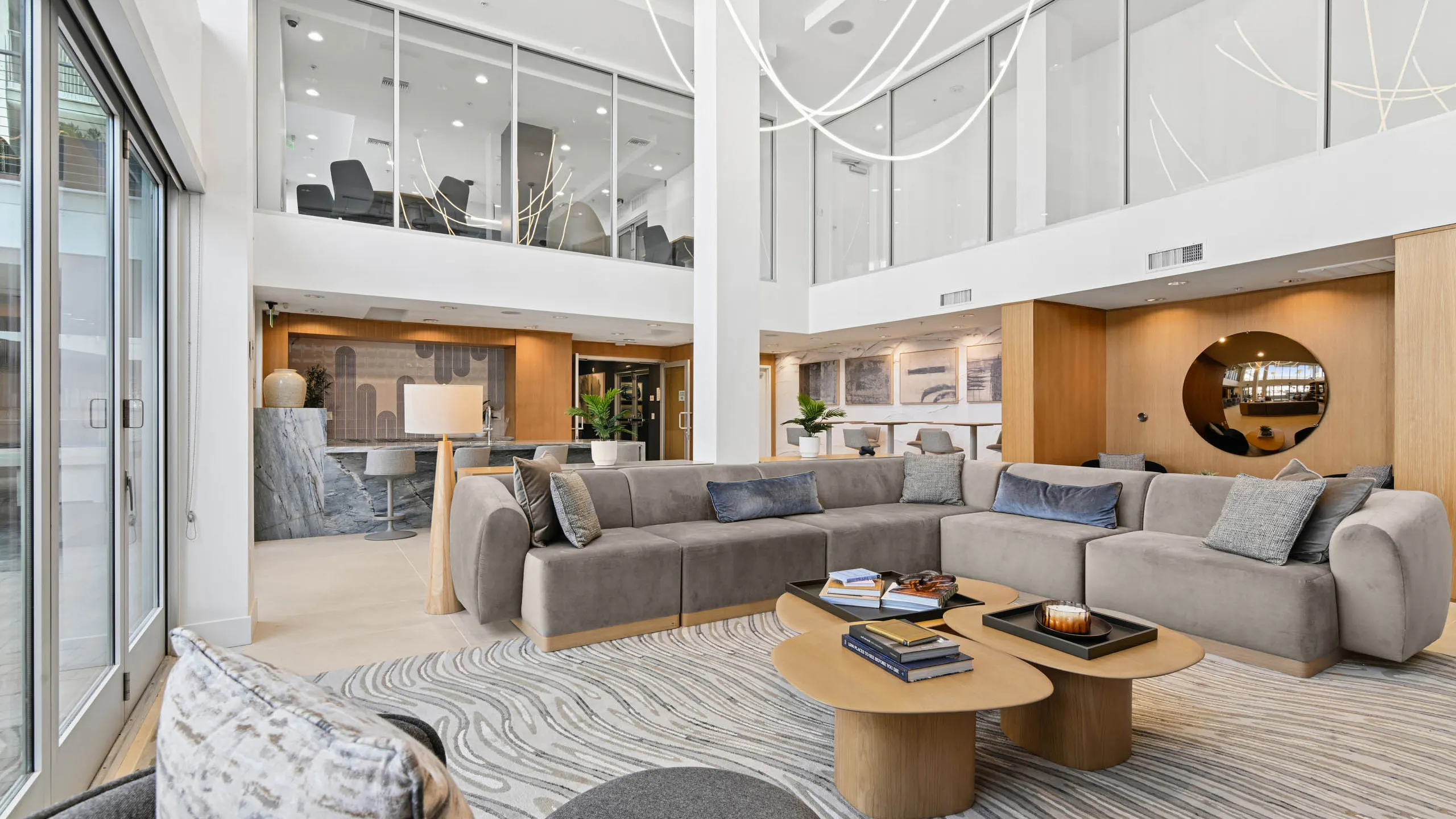 Clubroom at AMLI Lex on Orange with high ceilings, a large gray sectional, wood coffee tables, and a swirl-patterned rug, with a stone counter with stools and wood-paneled walls.