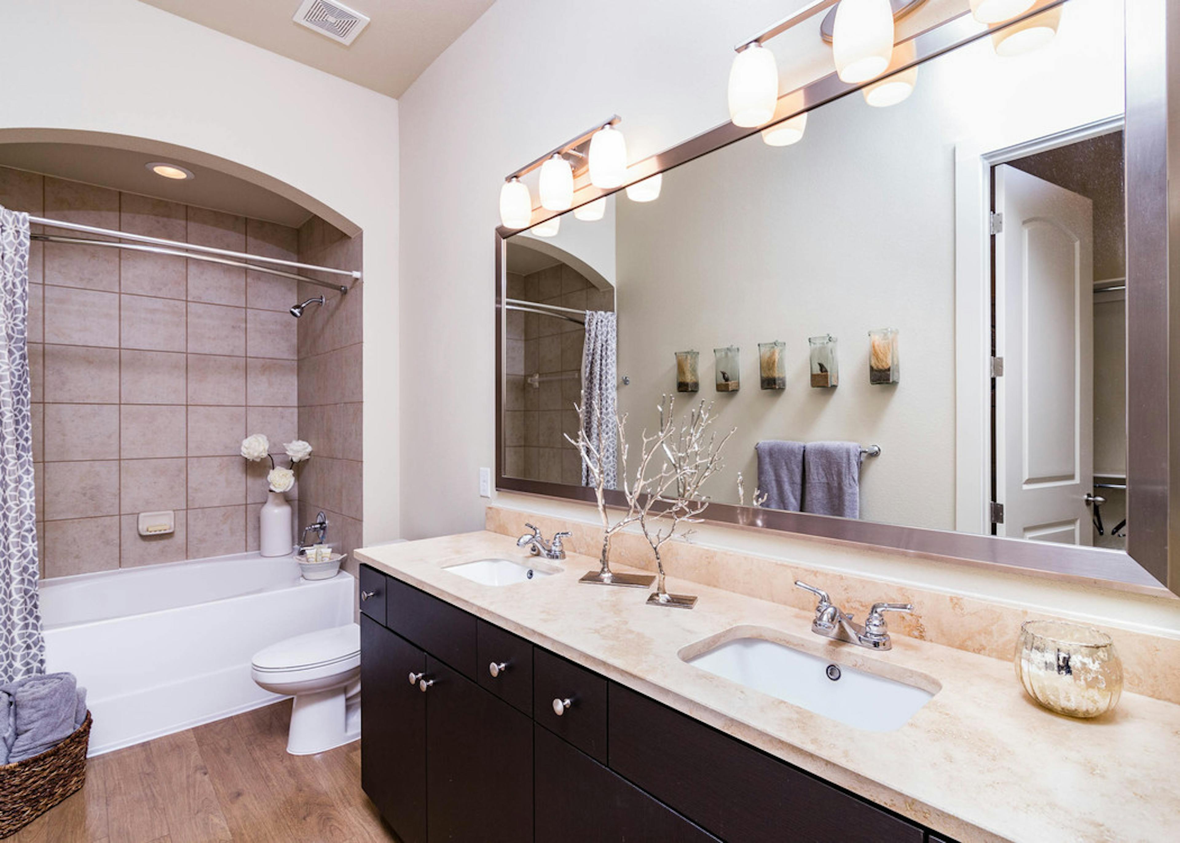 A bathroom at AMLI Ridgegate apartments with a granite counter top with two sinks and a large mirror with view of the shower