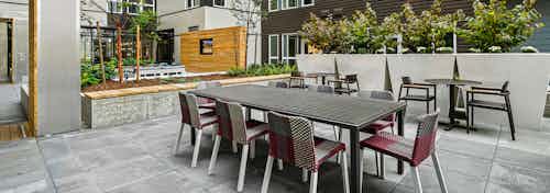 Outside courtyard with 3 gray tables and chairs surrounded by planters and trees at AMLI Spring District apartment building