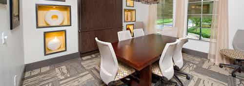 AMLI North Point media room with patterned carpet and long wooden desk with white swivel office chairs facing a large window
