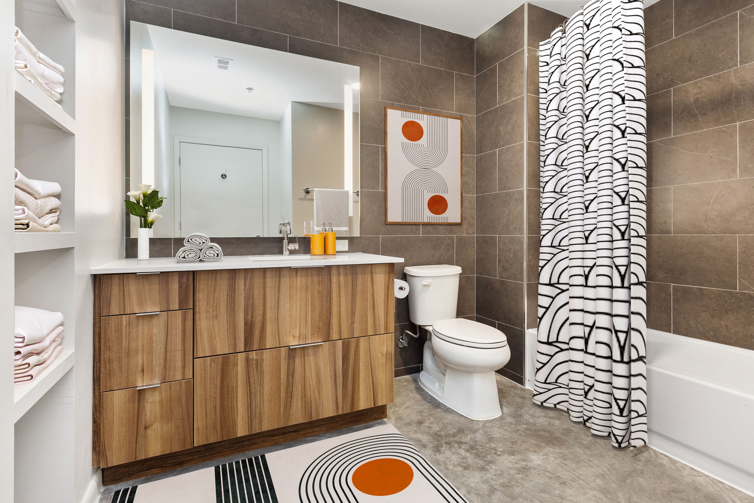 View of bathroom with wood vanity with large mirror above and white toilet and bathtub with geometric curtain at AMLI on 2nd