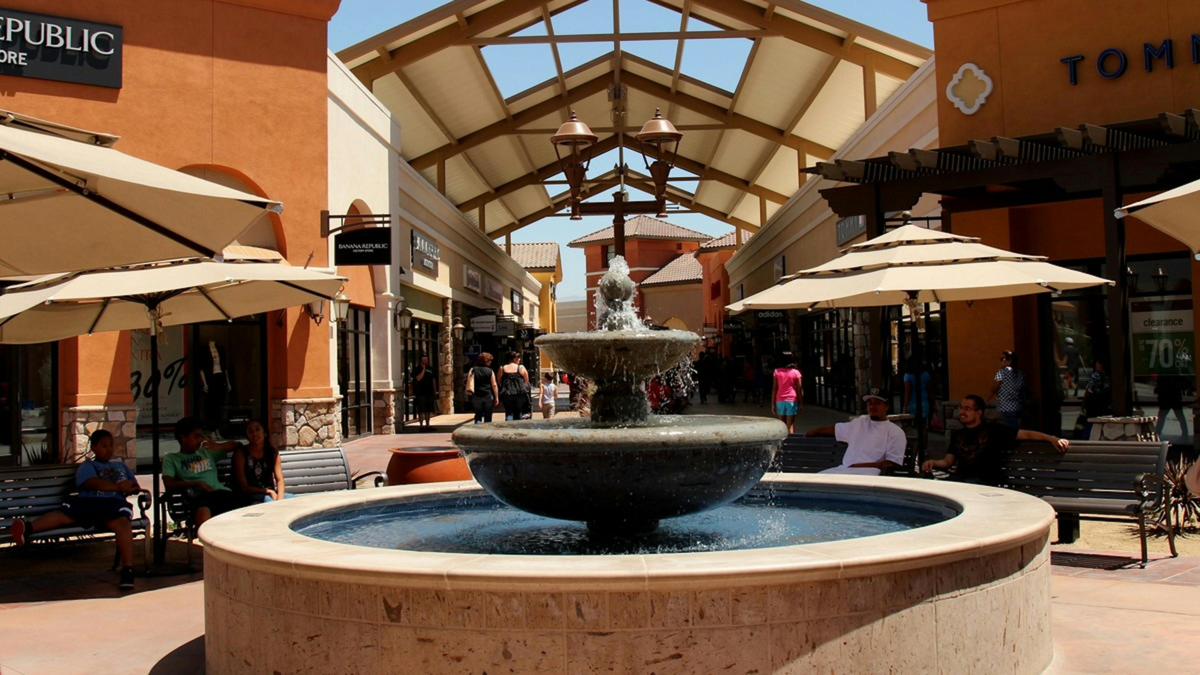 Exterior daytime view of Camarillo premium outlets shopping center with round three tier contemporary fountain and umbrellas