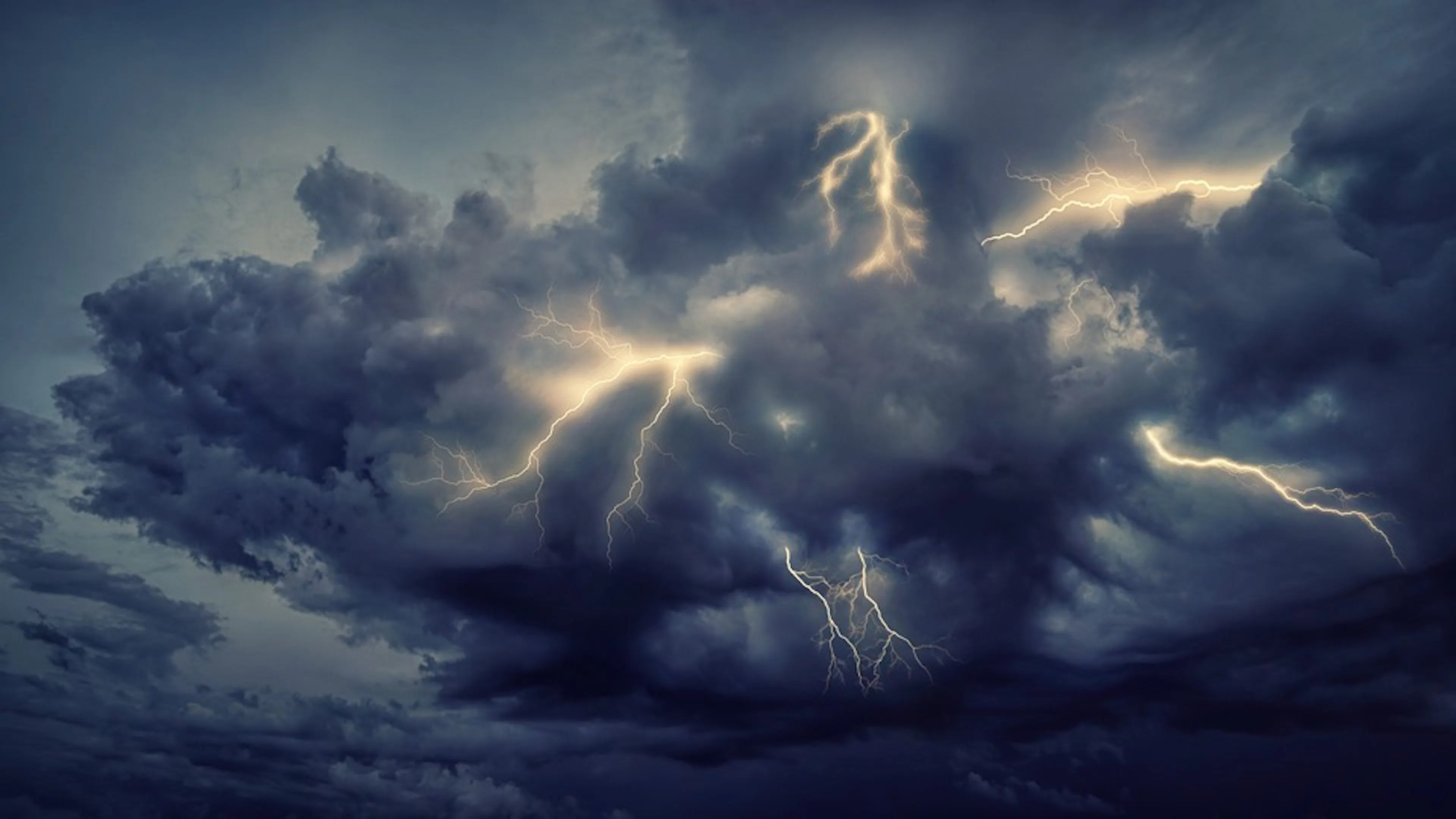 A dark thundercloud against a grey sky with strikes of lightning leaving from the center