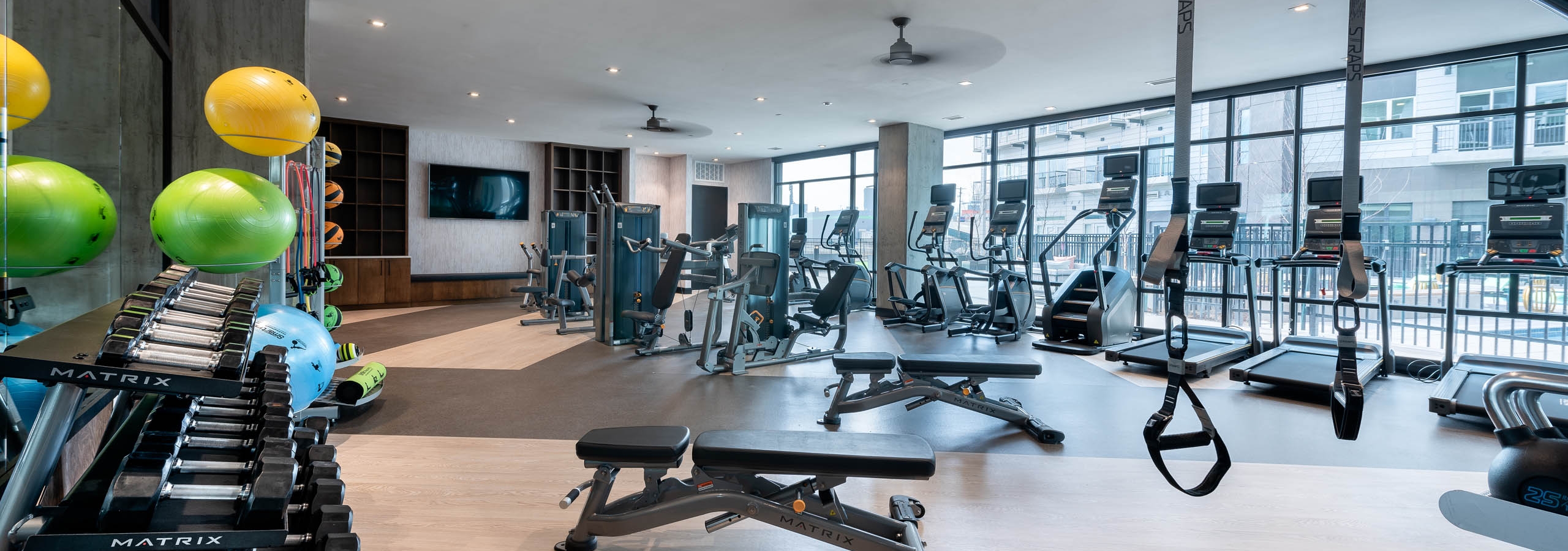 AMLI Art District fitness center with weights and cardio machines and a television and cabinets and floor to ceiling windows
