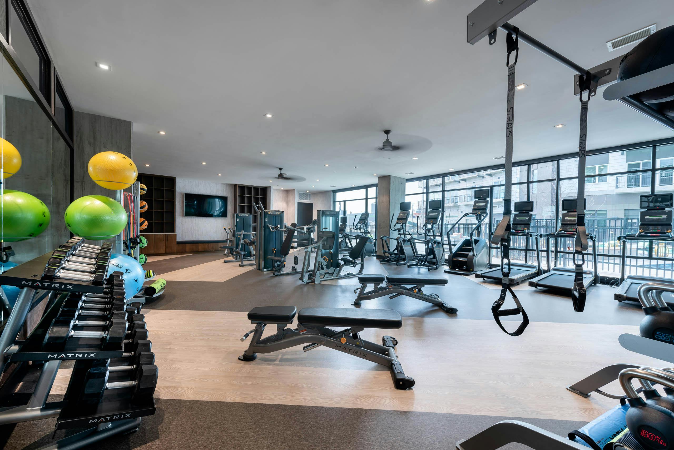 AMLI Art District fitness center with weights and cardio machines and a television and cabinets and floor to ceiling windows 